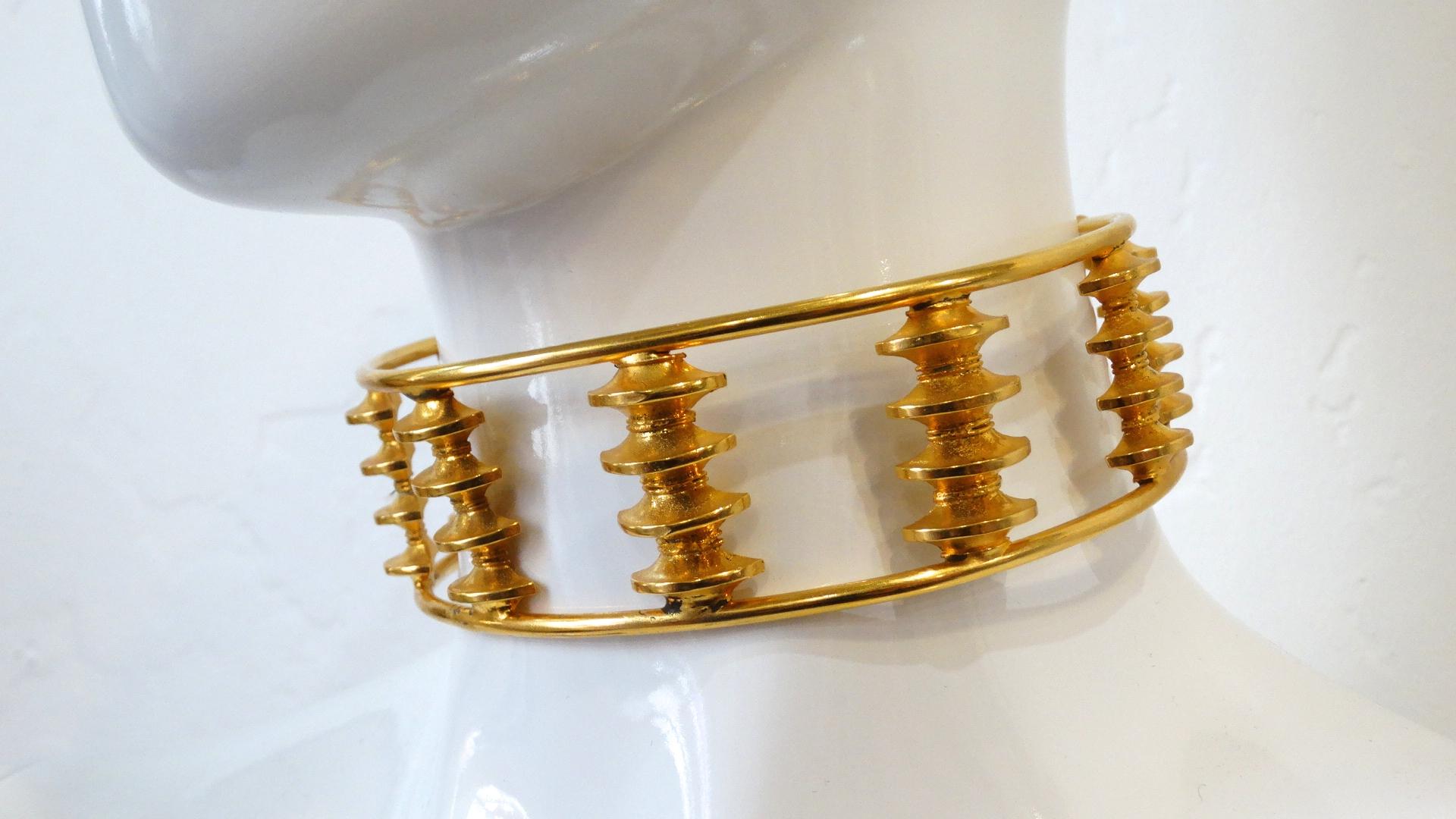 The Perfect Choker To Elevate Your Look Is Here! Circa 1970s, this William de Lillo statement choker is a U shape for easy wear and is plated gold. Features tiered columns around choker which resemble the curved roofs found in Japanese Buddhist