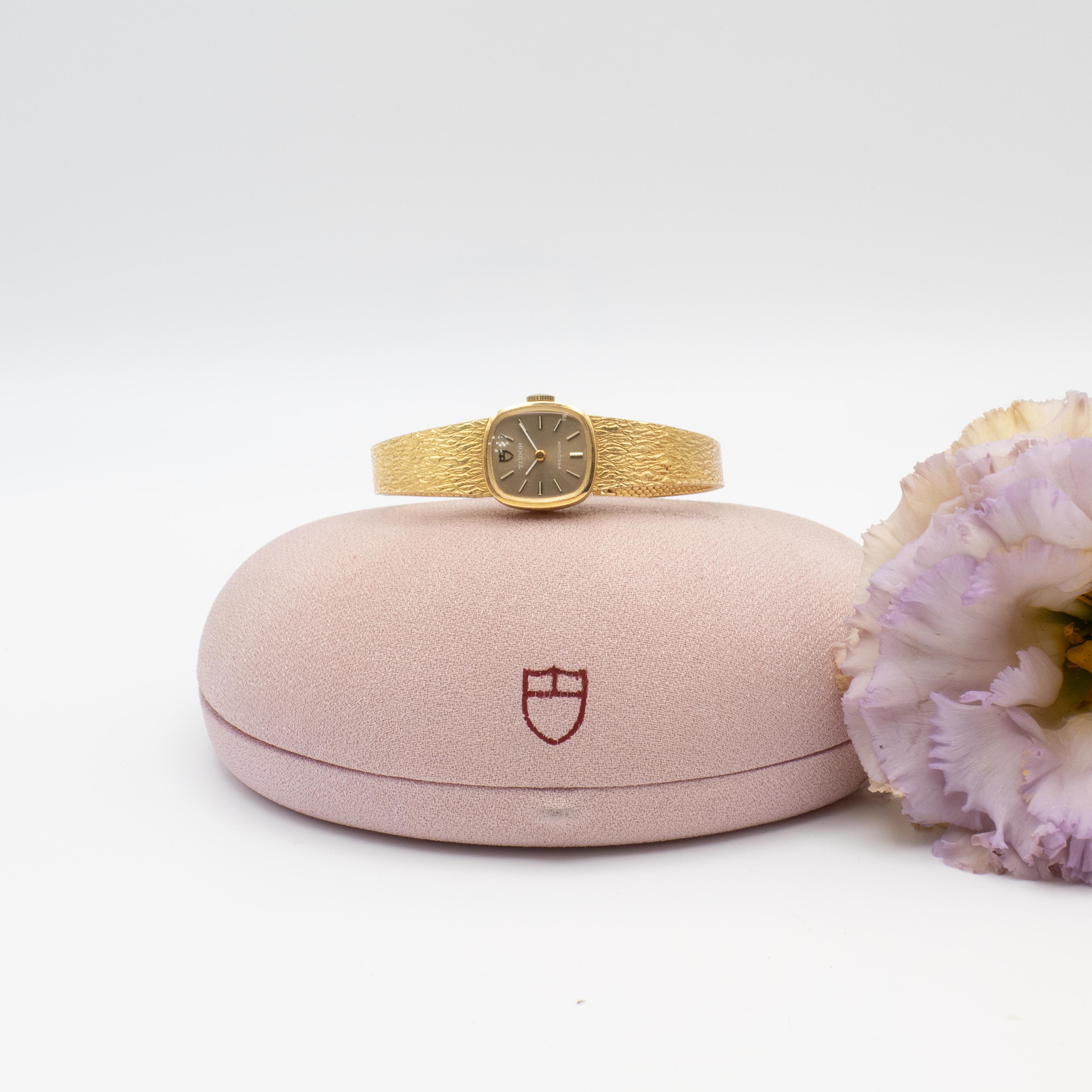 1970s Tudor 18K yellow gold ladies watch with 18K yellow gold bracelet and original presentation box. Swiss hand wind movement, cushion square face, gold case, gold band has a textured finish

Measurement:
Fits wrists 6-6.25