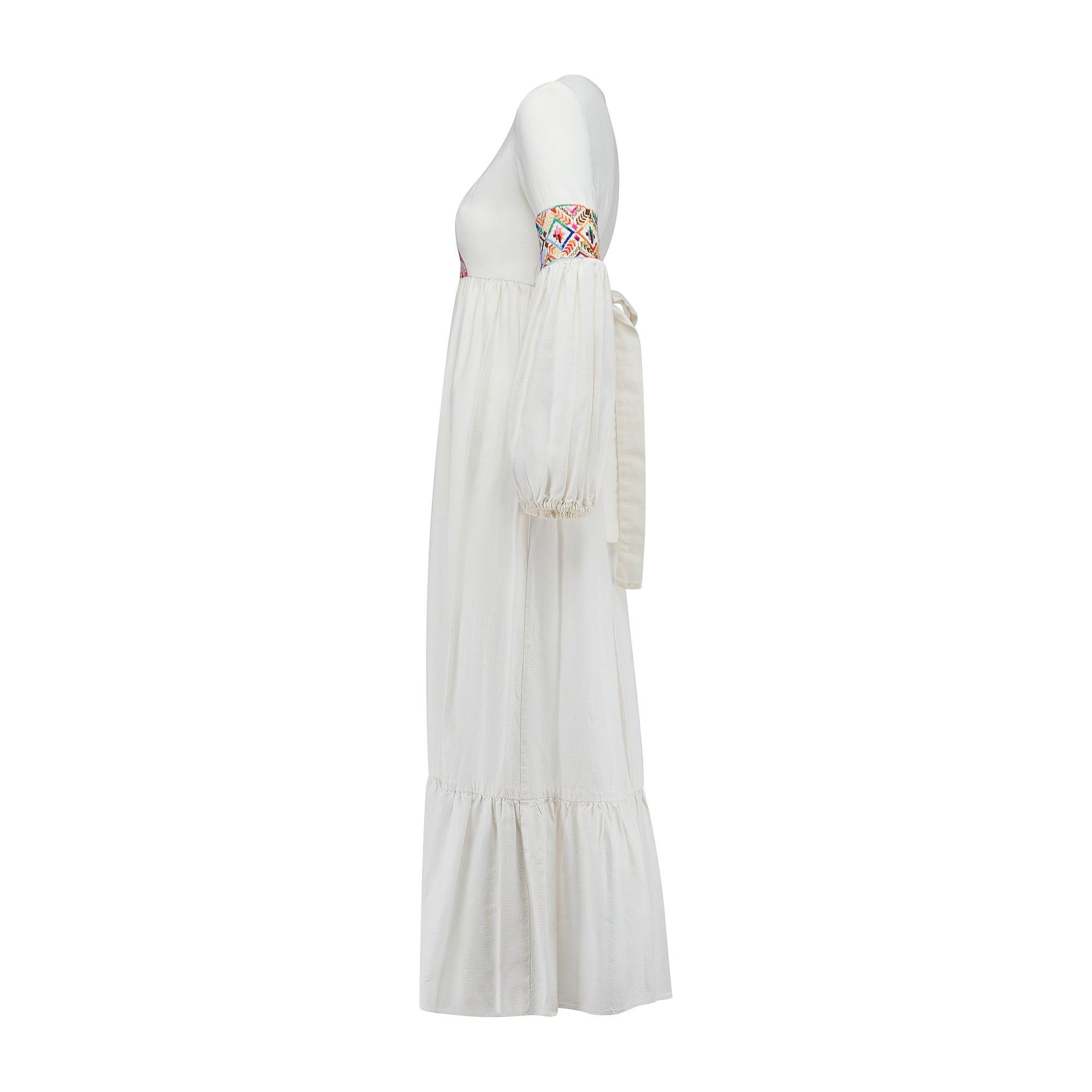 This dress was created in the 1970s by Young Edwardian, a collectible American vintage label which drew inspiration from antique clothing designs. Crafted from a thick white linen, it is tailored to a maxi-length with long bell-sleeves which are