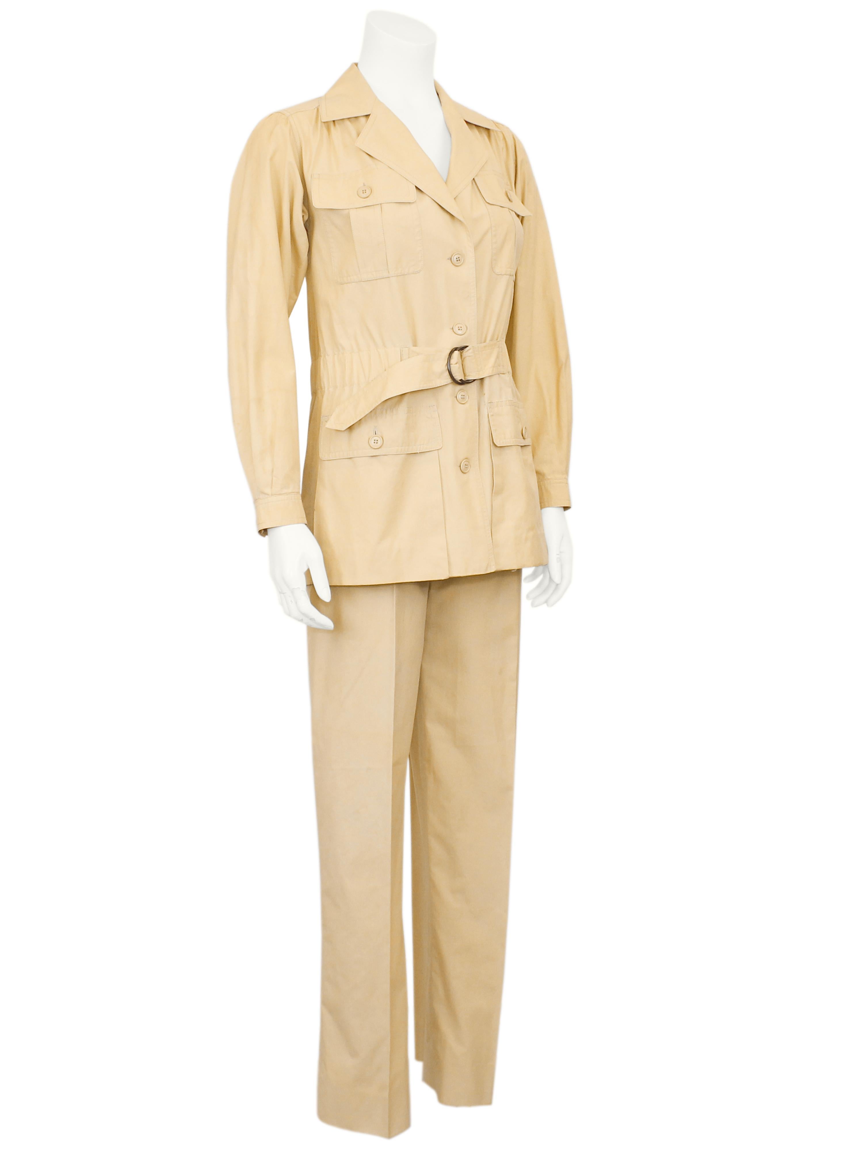 Iconic 1970s Yves Saint Laurent beige cotton safari jacket and trouser suit. The jacket is safari style with cargo pockets at the bust and hips and a cinched belt at the waist with a metal D ring closure. The trousers are high waisted and straight