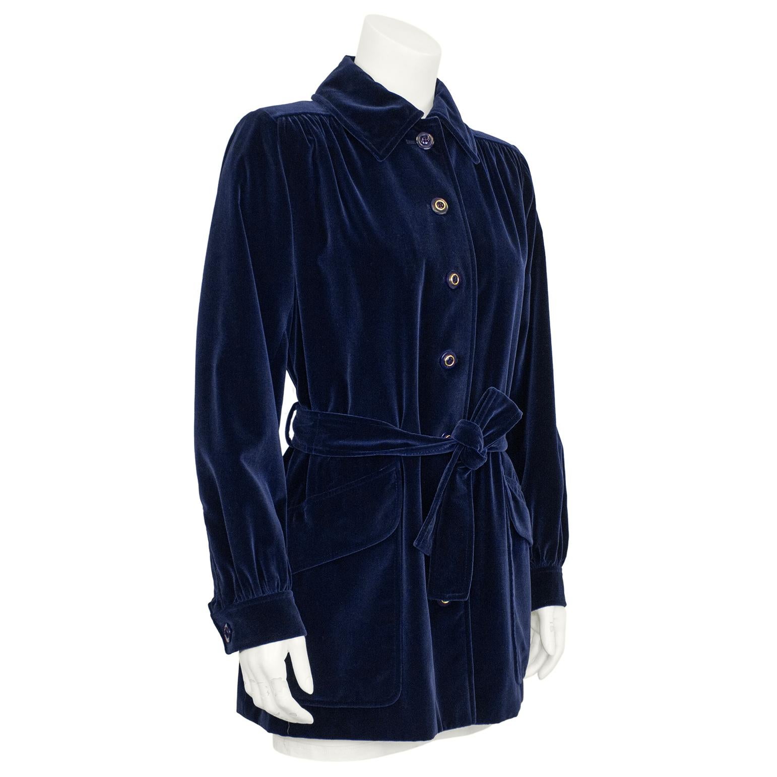 1970s Saint Laurent Rive Gauche navy velvet jacket. The soft velvet is in perfect condition with navy and gold buttons fastening down the front. Two large cargo style top flap pockets on the hips, the long line jacket has a matching belt that ties