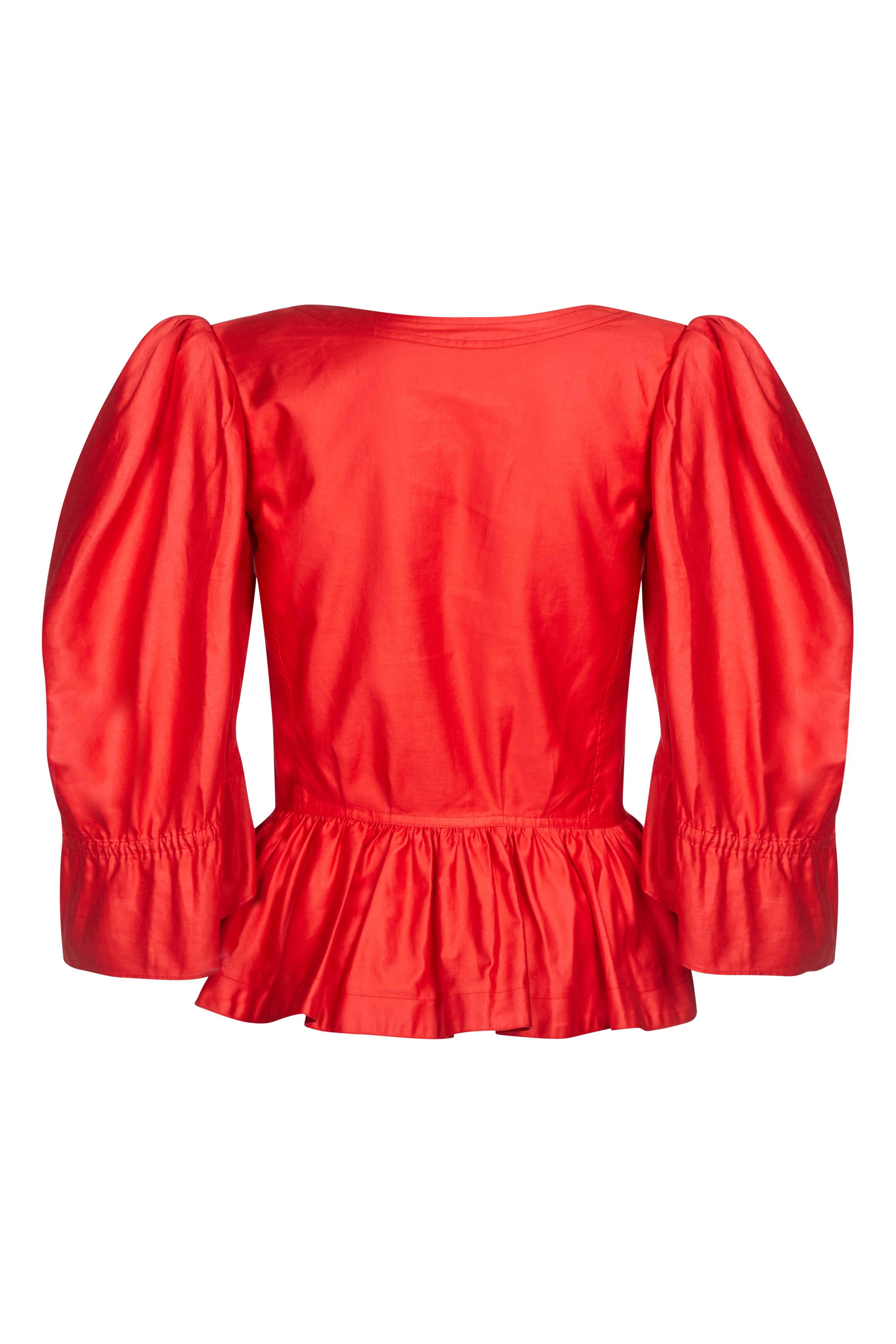 This vibrant 1970s Yves Saint Laurent red polished cotton blouse is guaranteed to turn heads. The deep red colour, bold puff shoulder feature, lavish bell sleeves and peplum detail makes this something of a statement piece. The bodice is beautifully