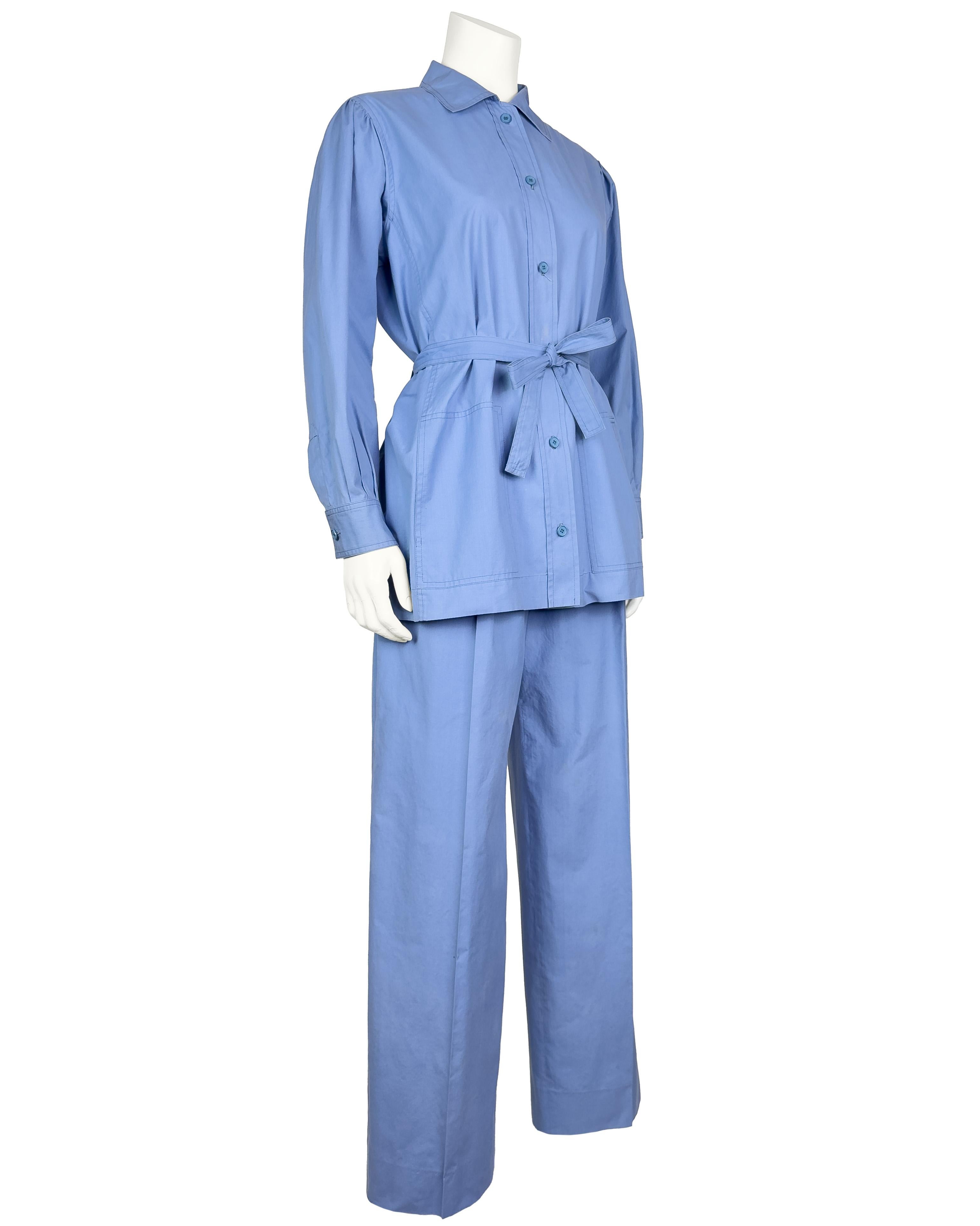 Iconic 1970s Yves Saint Laurent cornflower blue cotton safari jacket and trouser suit. The jacket is safari style with cargo pockets at the bust and hips and a cinched belt at the waist with a metal D ring closure. The trousers are high waisted and