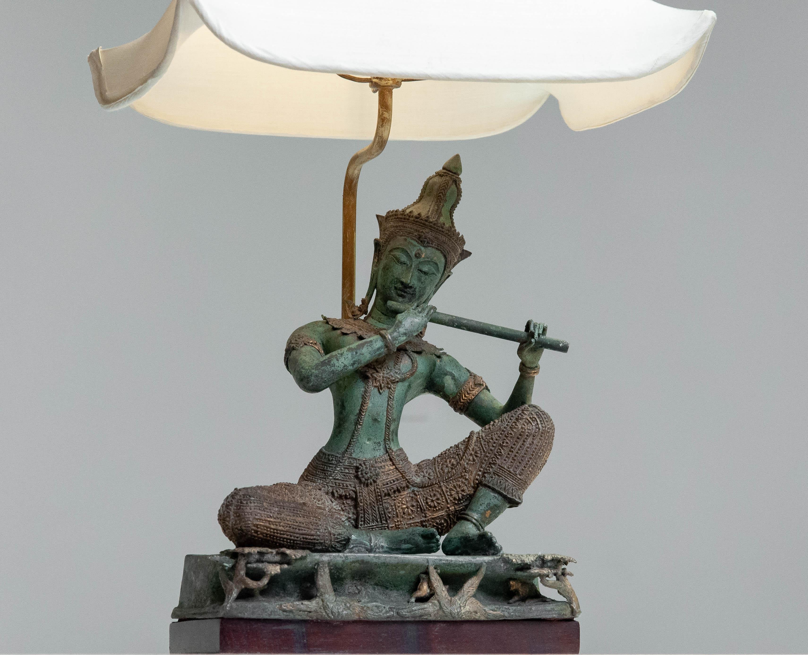 Una splendida lampada da tavolo in bronzo con un'intricata figura di musicista tailandese in posa seduta.

Materiale: Bronzo fuso con dettagli dorati
Design/One: Divinità tradizionali ispirate al sud-est asiatico che suonano uno strumento