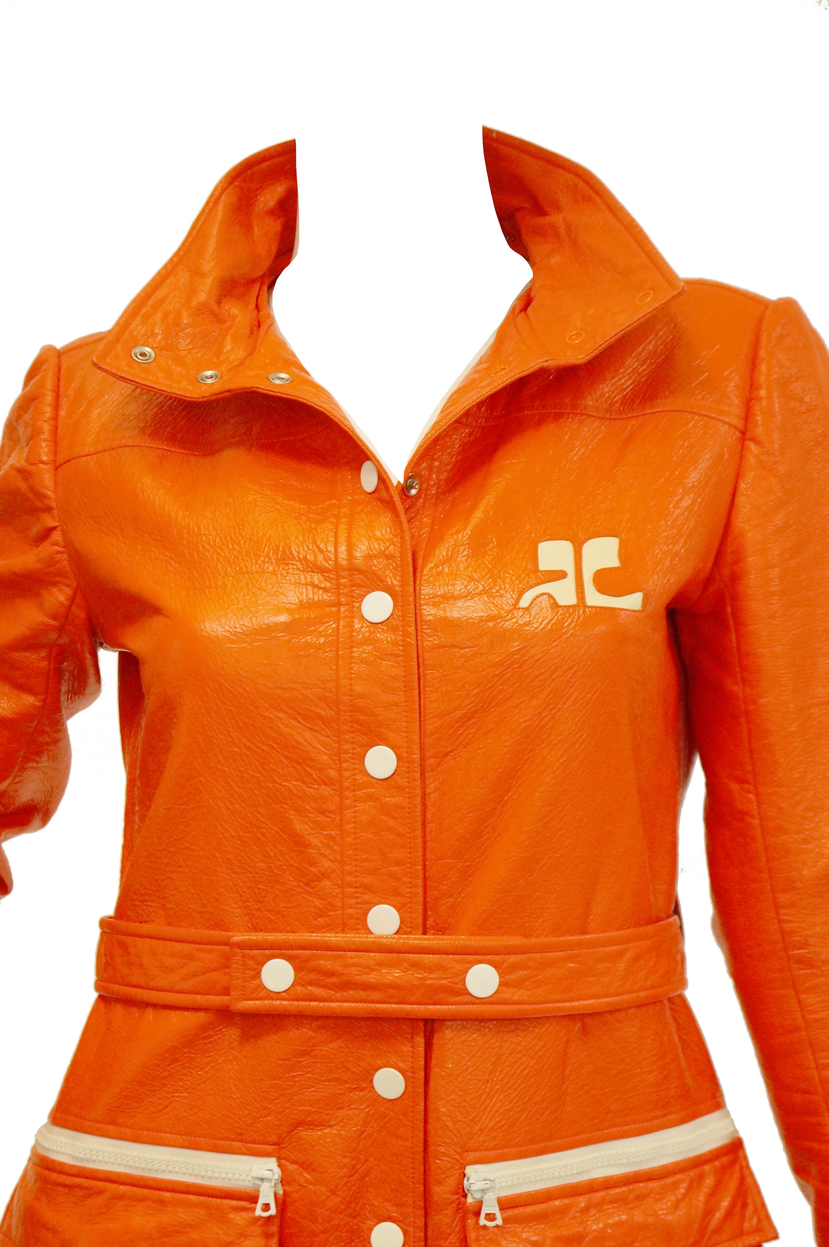 Incredible absolutely astounding bright orange vinyl coat by André Courrèges.  We cannot get over this oh - so - mod trench coat! The coat is midi length, with long sleeves, and a high collar. The iconic Courrèges logo features prominently in white