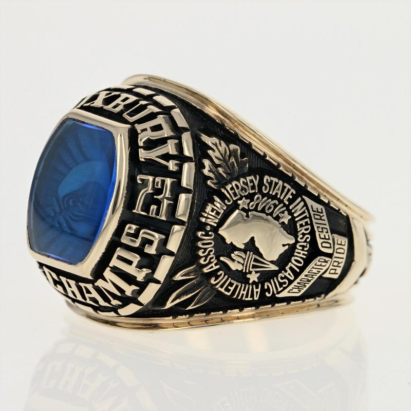 Crafted by Herff Jones in 10k yellow gold, this 1973 New Jersey State Interscholastic Athletic Association high school football championship ring features a gleaming synthetic blue spinel, which showcases an image of a football, that is framed by