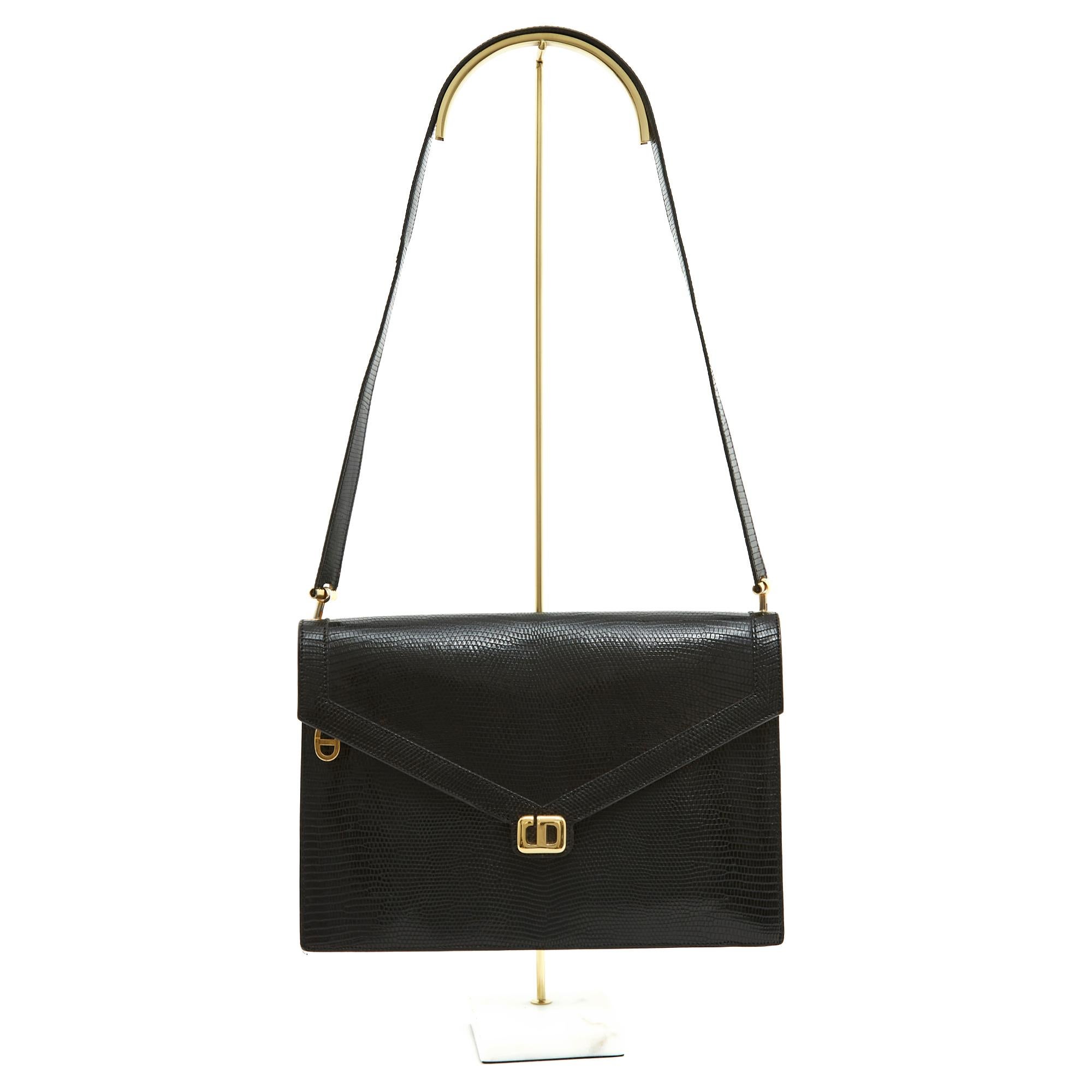 Christian Dior Tasche, bestehend aus einer kuvertförmigen Clutch aus schwarzer Eidechse, die mit einem Druckknopf unter dem Dior-Logo aus vergoldetem Metall verschlossen wird. Innen ist sie aus schwarzem Leder, mit einem kurzen, abnehmbaren