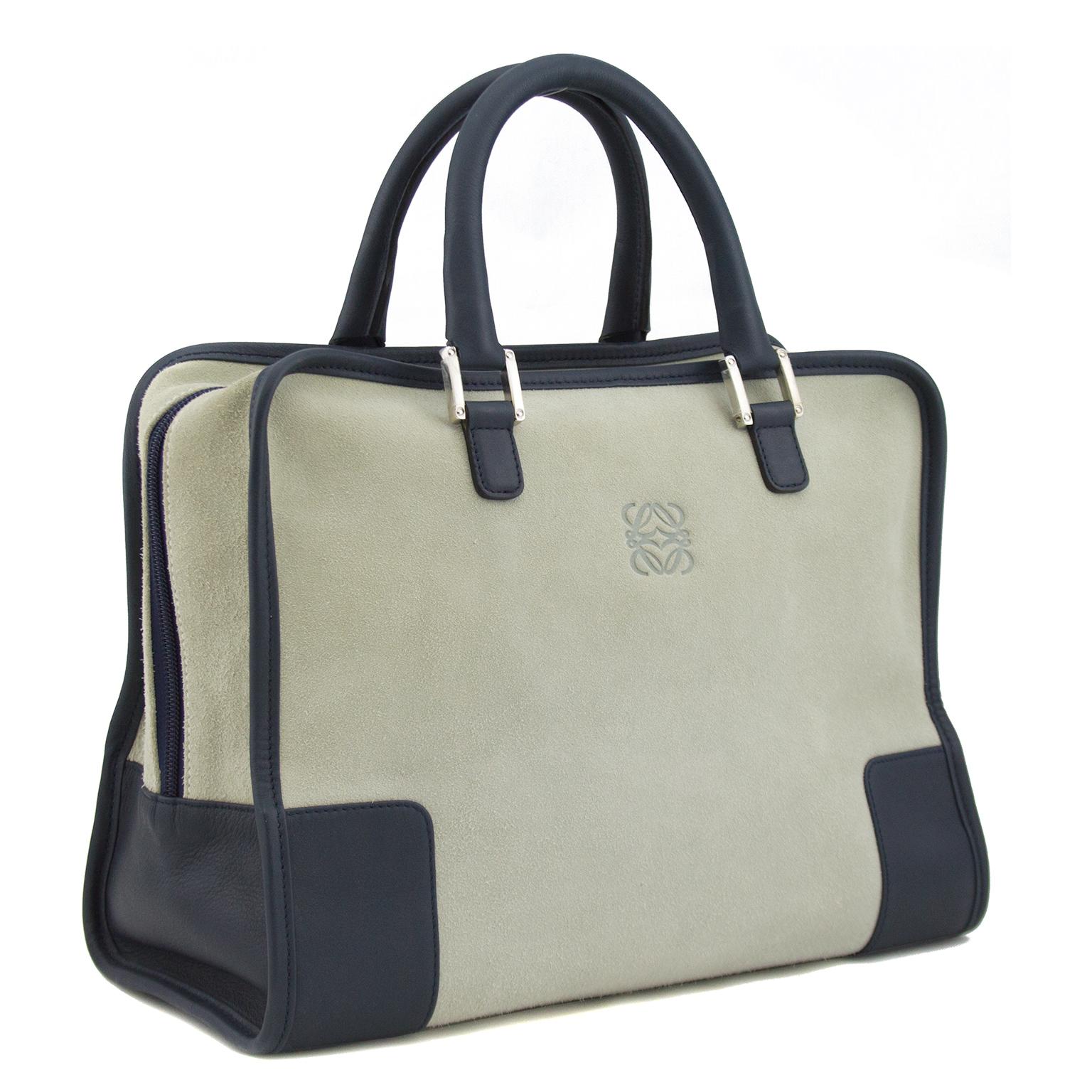 This authentic Loewe Amazona bag is crafted in greige suede with navy leather trim. A precursor to the This bag features dual-rolled leather handles, stamped logo at front, protective base studs and silver-tone hardware. Its zip closure opens to a
