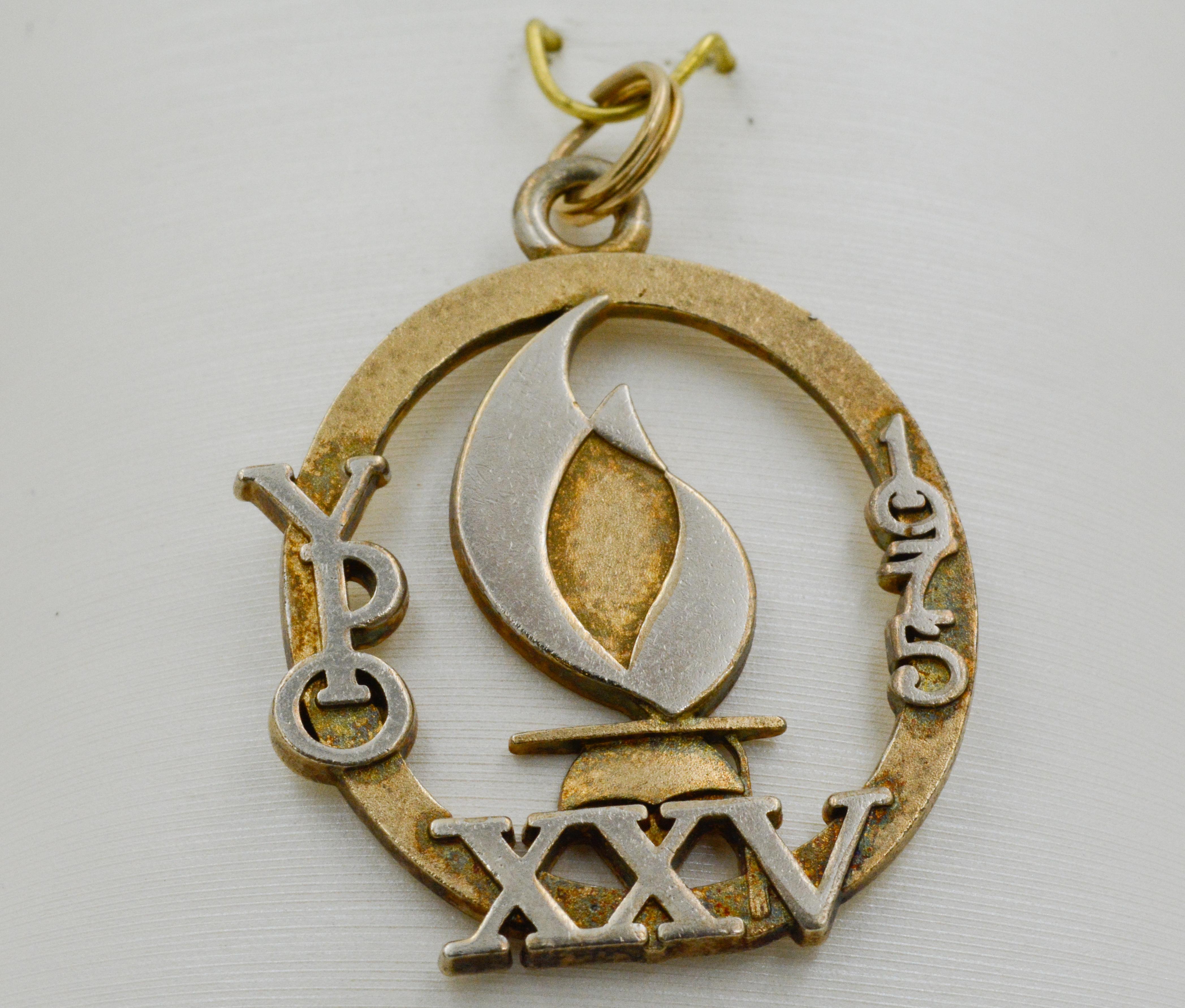 This charm is plated with sterling silver and yellow gold. The charm features a depiction of a flame over Roman numerals XXV. “YPO” and “1975” are incorporated into the charm’s frame, and they round out the regal look while also infusing the charm