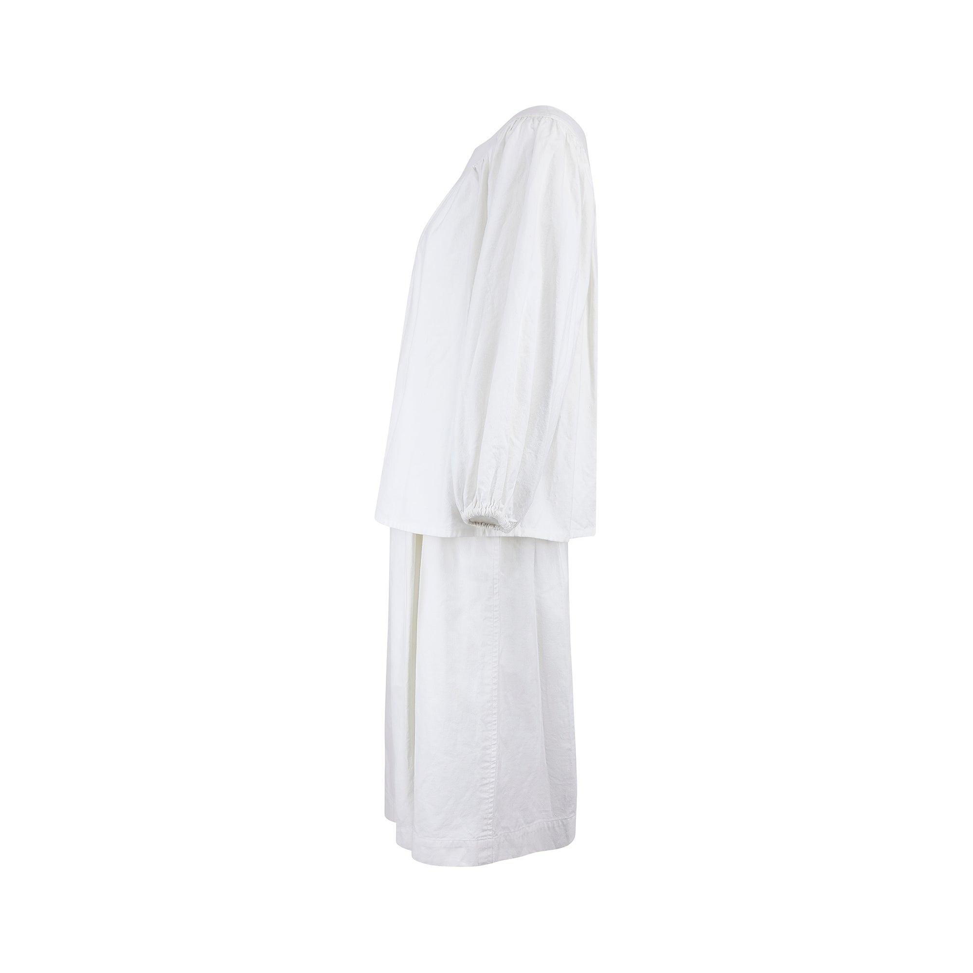 Dieses klassische Sommerensemble aus weißer Baumwolle stammt aus der Ready-to-Wear-Kollektion Frühjahr/Sommer 1975 von Yves Saint Laurent. Das Oberteil hat Ballonärmel und einen luftigen, lockeren Schnitt. Der elegante, weite Ausschnitt ist eine