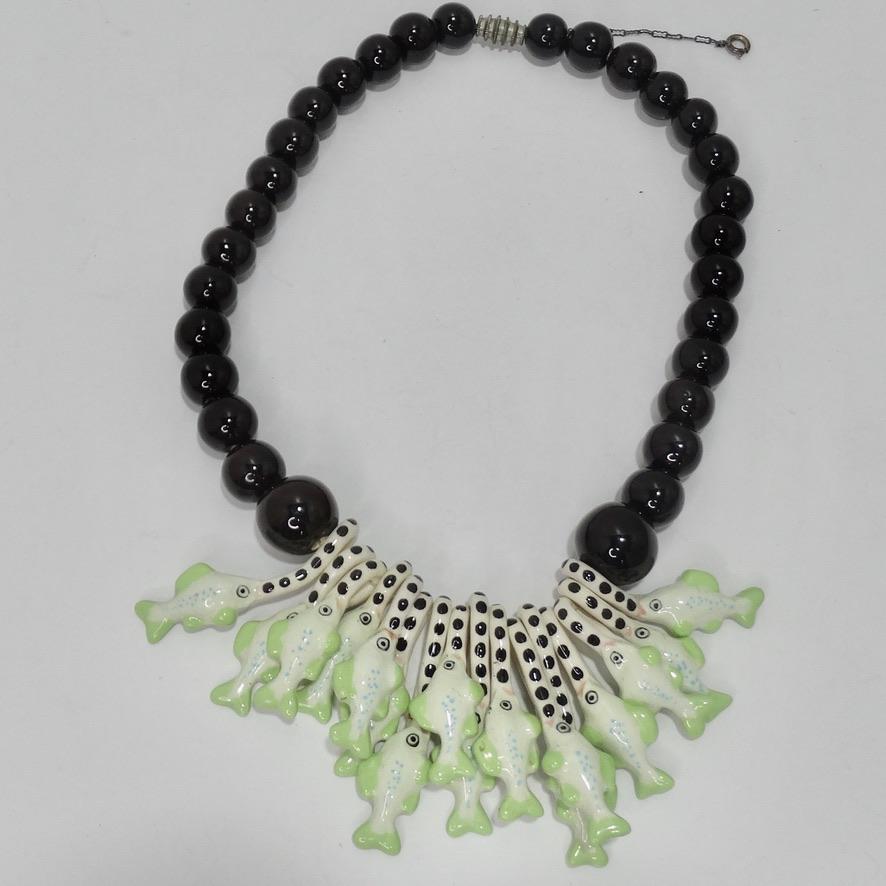 This 1976 Parrot Pearls charm necklace is the perfect statement piece to add to your collection! Chunky black beads are accompanied by a big arrangement of green, white, and black glass fish charms. Sits at a great medium length at the center of the