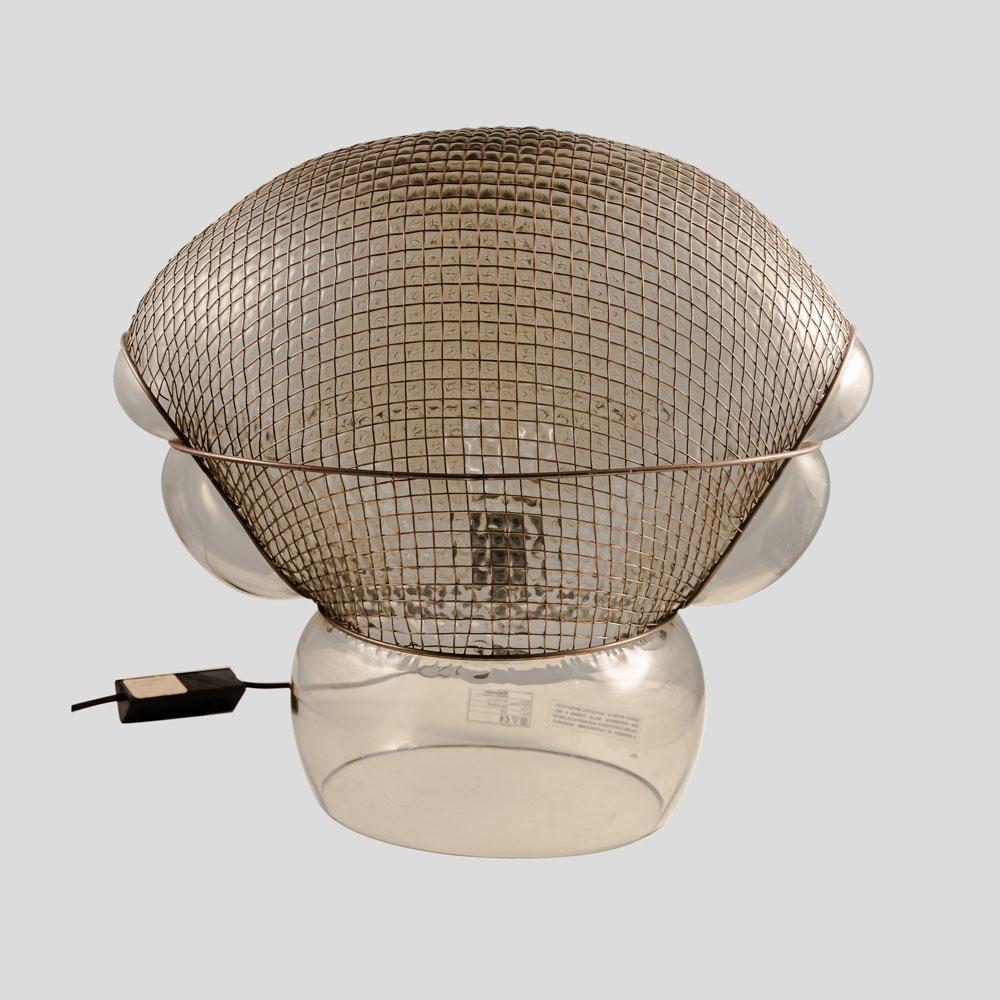 The Vintage Patroclo lamp is an authentic Italian design from 1976 by Gae Aulenti for Artemide. It features a body made of thick transparent bronze colored blown glass, with a diffuser that is partially covered by a unique irregular rhomboid metal
