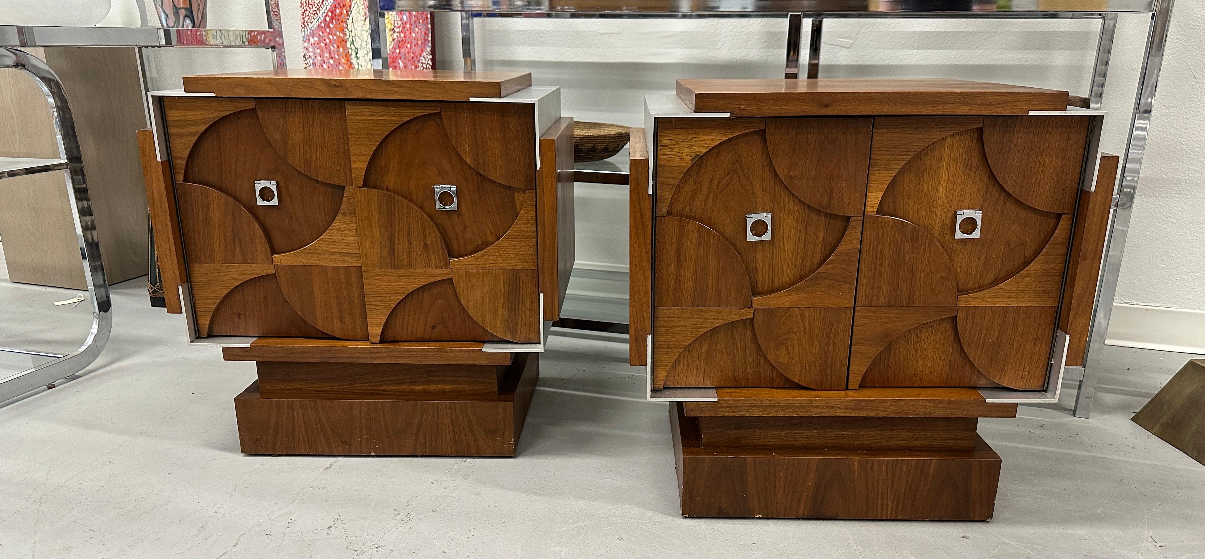 A pretty set of walnut nightstands in the brutalist style by the Canadian Furniture Tobago. Beautifully sculpted fronts with satin aluminum inserts. They are stamped on the bottom Made In Canada July 18 1976. 
There are holes on the interior sides