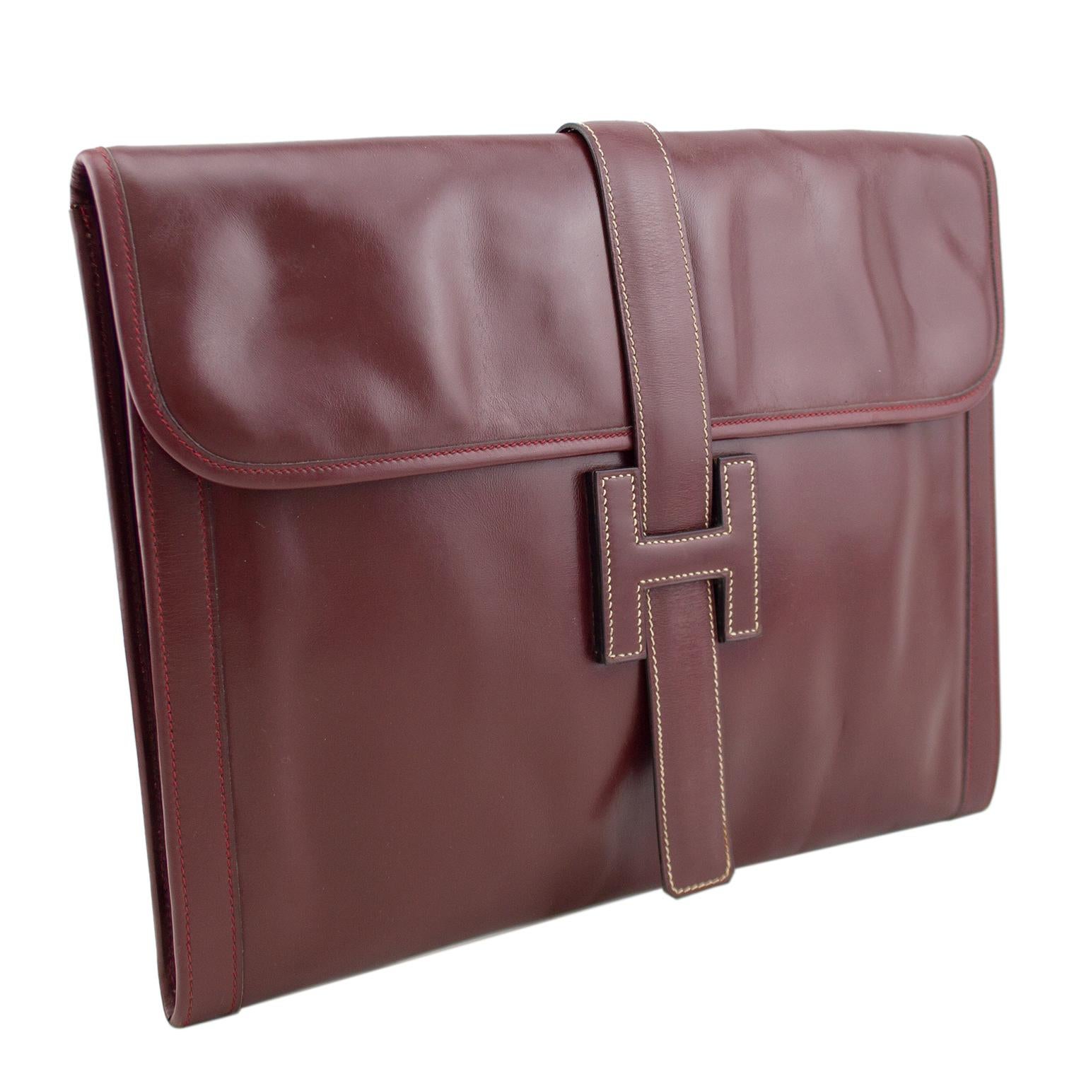 A classic day-to-night clutch that never goes out of the style, this Hermés Jige dates from the same year as its creation, 1975. This maroon leather version has the H style leather clasp on the front with a top flap opening. Finished with cream and