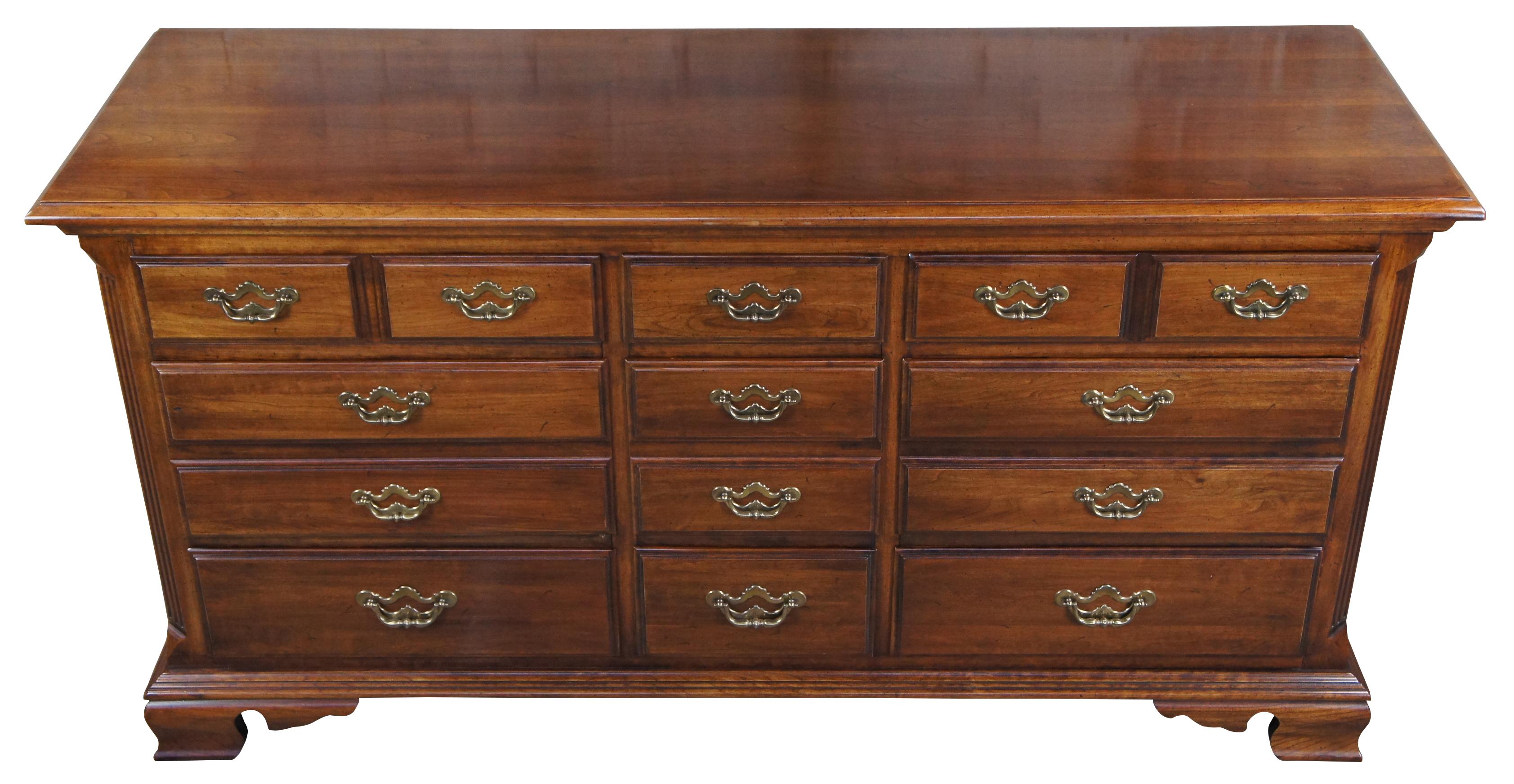 Thomasville Collectors Cherry Georgian style triple dresser, circa 1978. Features a long rectangular cherry case with nine dovetailed drawers and brass bale hardware. Includes a naturally distressed frame, tall mirror with open pediment and
