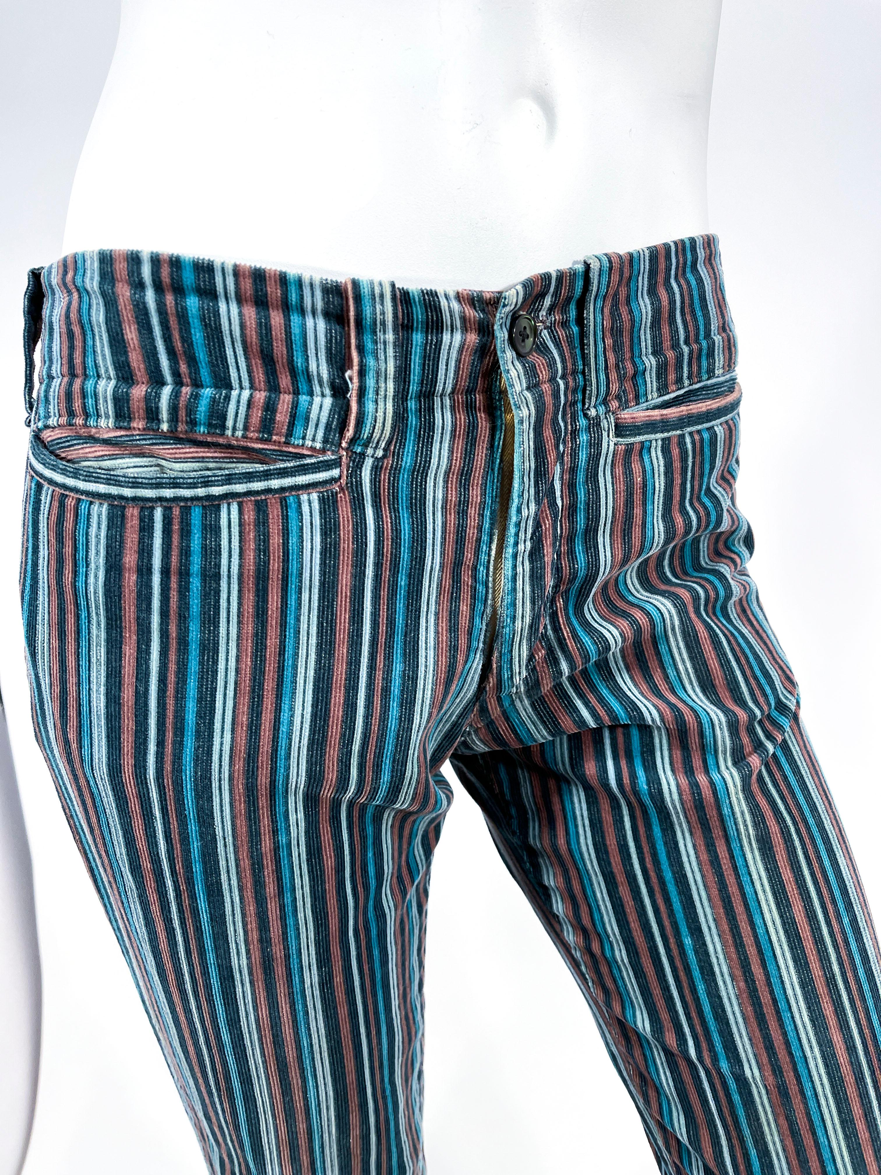 1979 Andrew Yiannakou corduroy featuring vertical stripes in teal, tan, and light blue. The low rise hip hugger waist has two front pockets, matching belt loops, and metal zip fly. Note these pants are meant to be worn on the hip