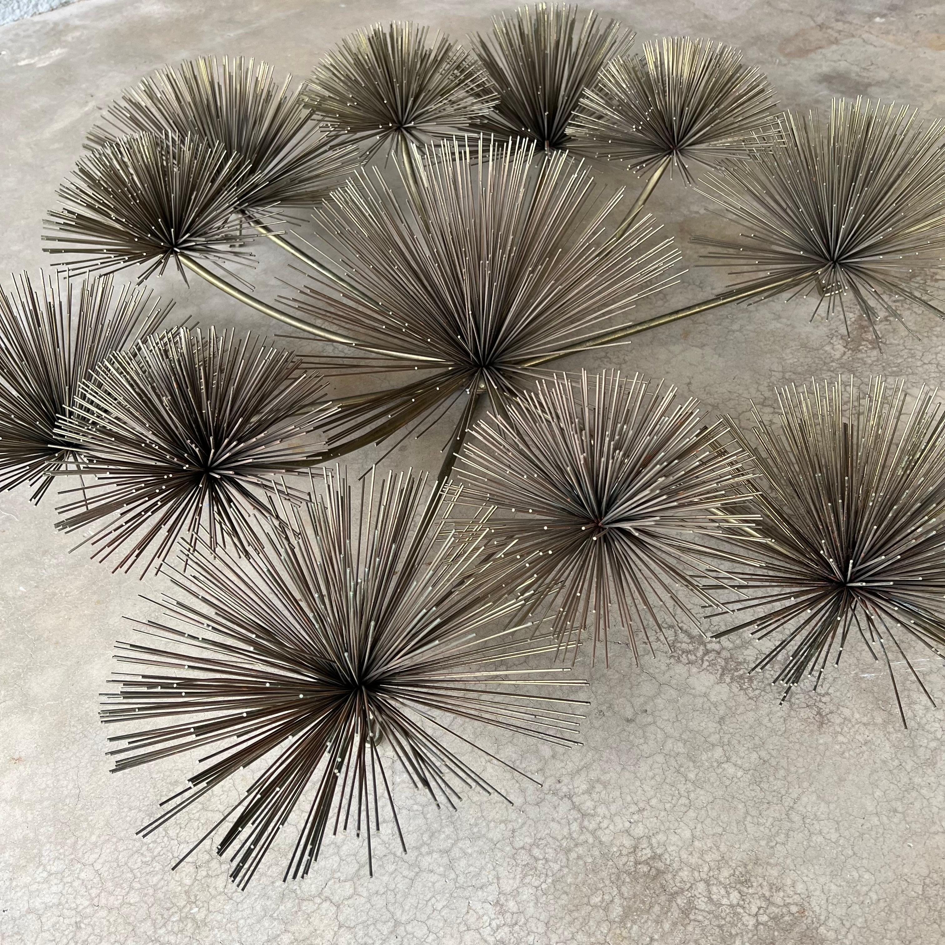 1979 C. Jeré Artisan House urchin or pom pom brass wall art. This is the much less common massive round version and measures about 40” wide and 10” deep. It features 12 urchins on curved stems. It is signed and dated with age-appropriate wear.