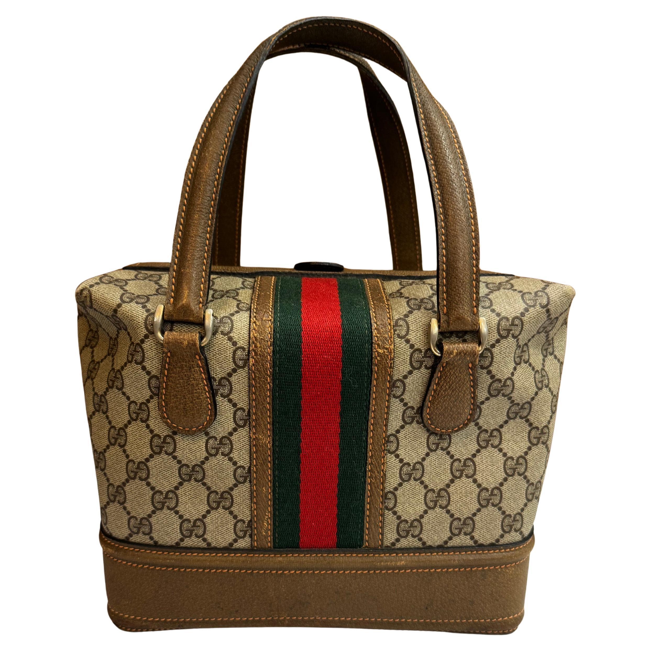 This small vintage GUCCI Web vanity trunk bag is crafted of brown GG monogram canvas and pigskin leather in dark brown decorated with Gucci’s iconic red/green stripe. Top push lock opens to a leather  interior in beige featuring a leather strap to