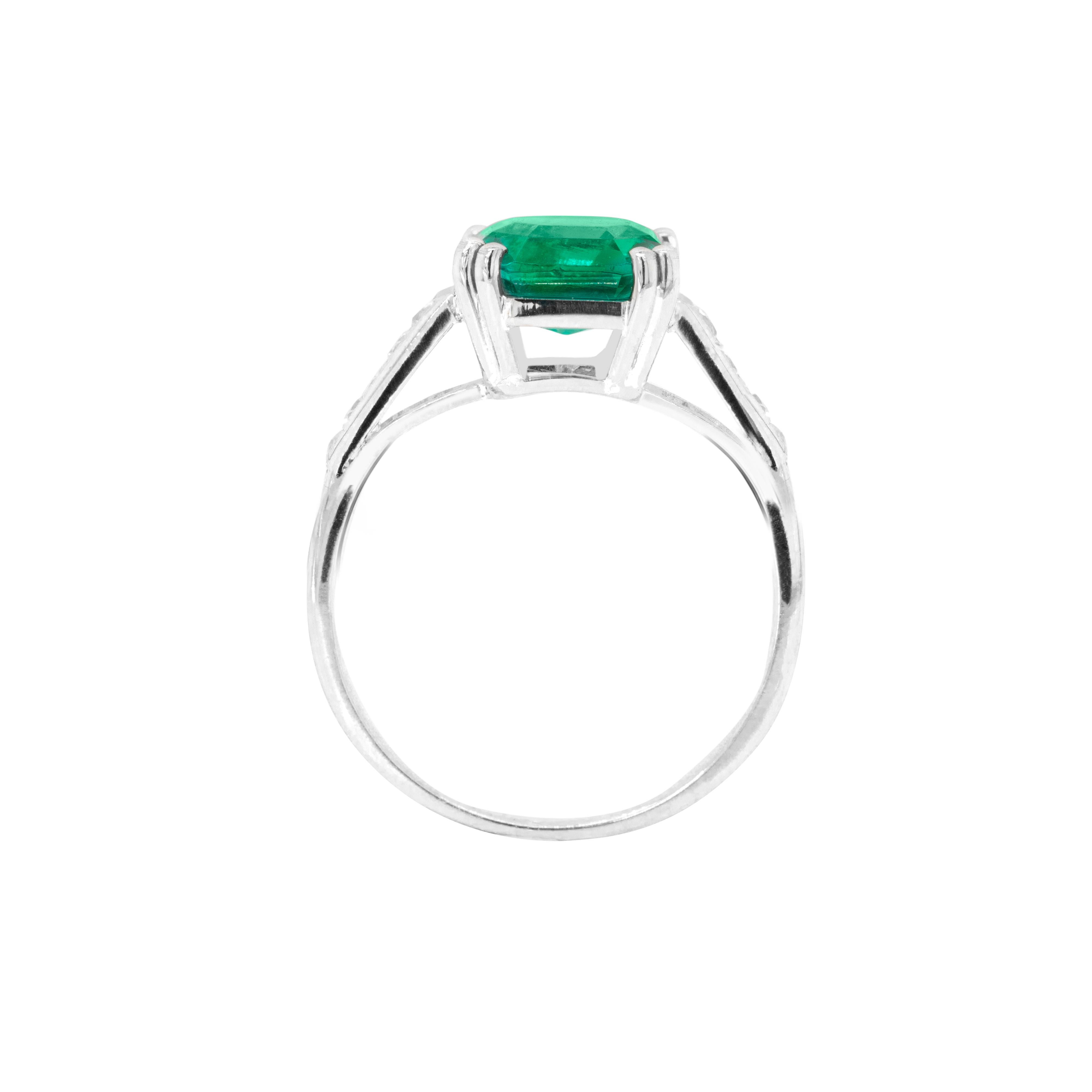 This gorgeous engagement ring features an exquisite 1.97 carat square emerald cut Colombian emerald mounted in a four double claw, open back setting. The vibrant gemstone is beautifully accompanied by five French cut diamonds, channel set on either