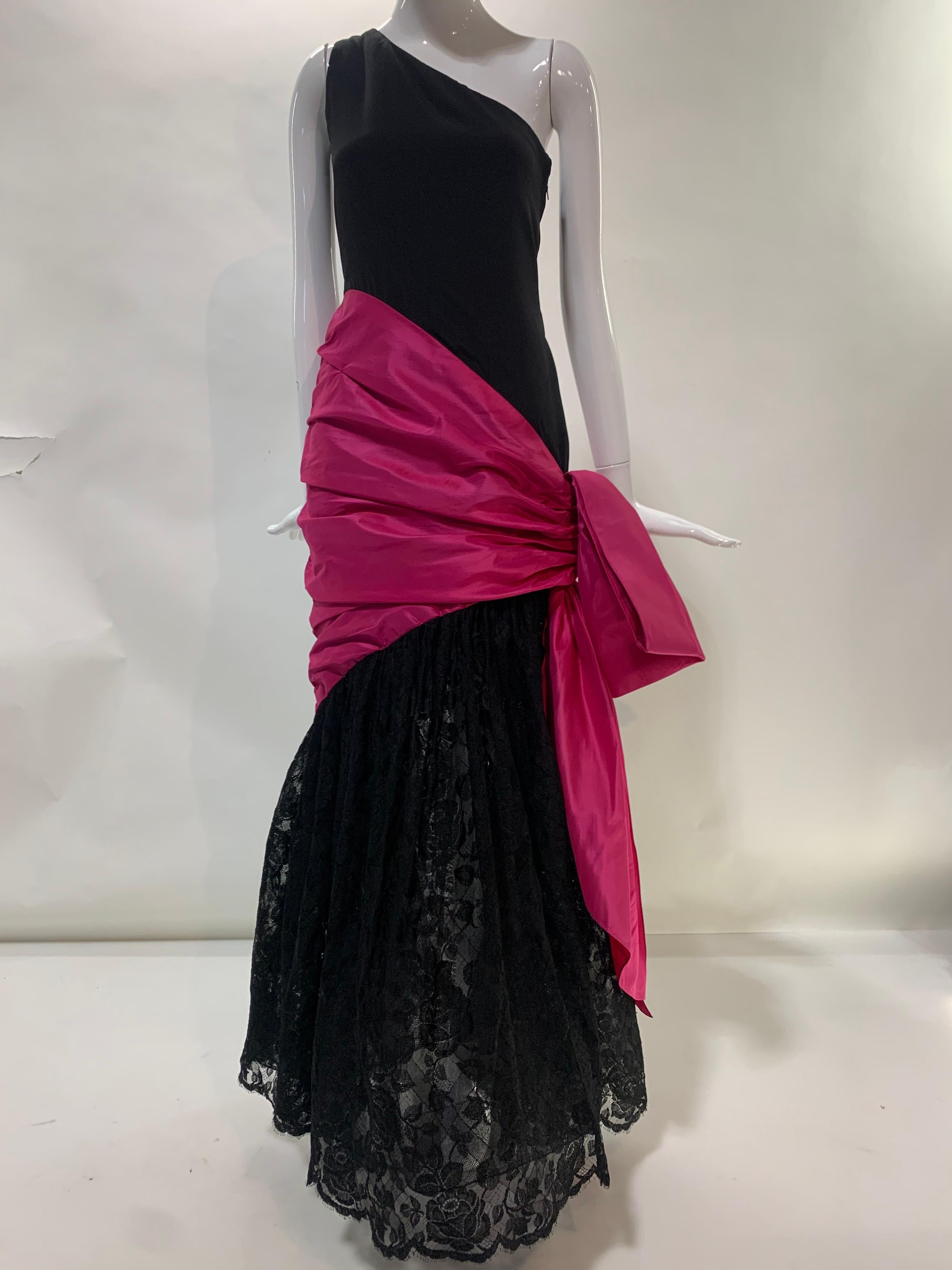 A fantastic late 1970s to 1980 Bill Blass black silk crepe one-shoulder evening gown with a black lace flared skirt. At hip is a wide band of fuchsia silk taffeta side-slung structured bow, evoking a Spanish dancer's shawl tied about the waist.