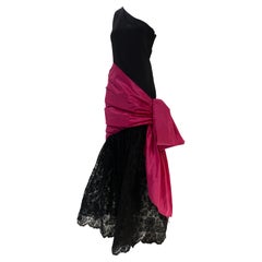 1980 Bill Blass, abito monospalla in crepe di seta nero con gonna in pizzo e fiocco fucsia