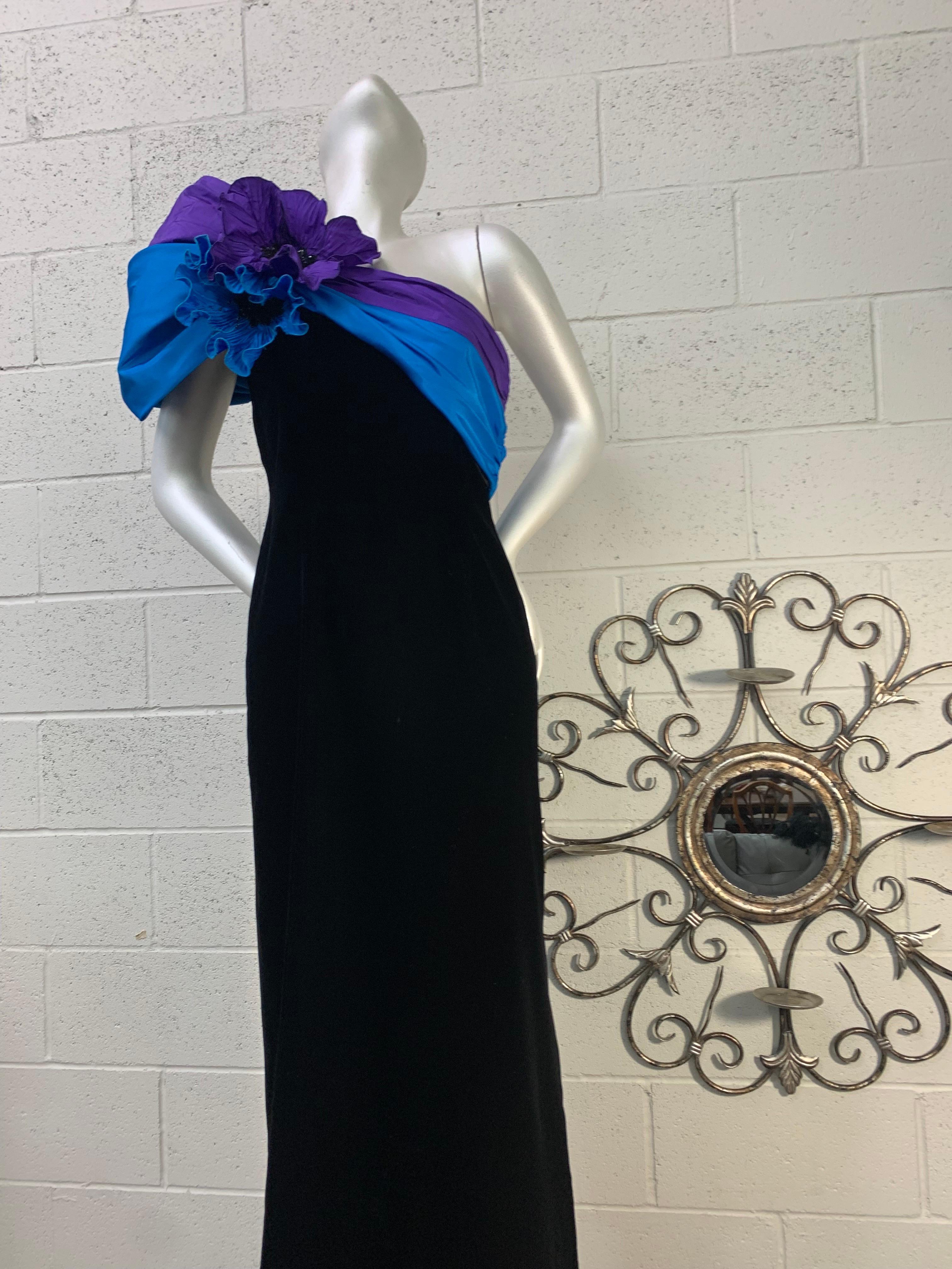 A stunning 1980s Eugene Alexander black velvet column gown with a vivid cobalt and purple silk sash draped across one shoulder and bust, gathered to a large rosette with boning at shoulder flourish. Side slit in skirt. Fully lined. US modern size 6.