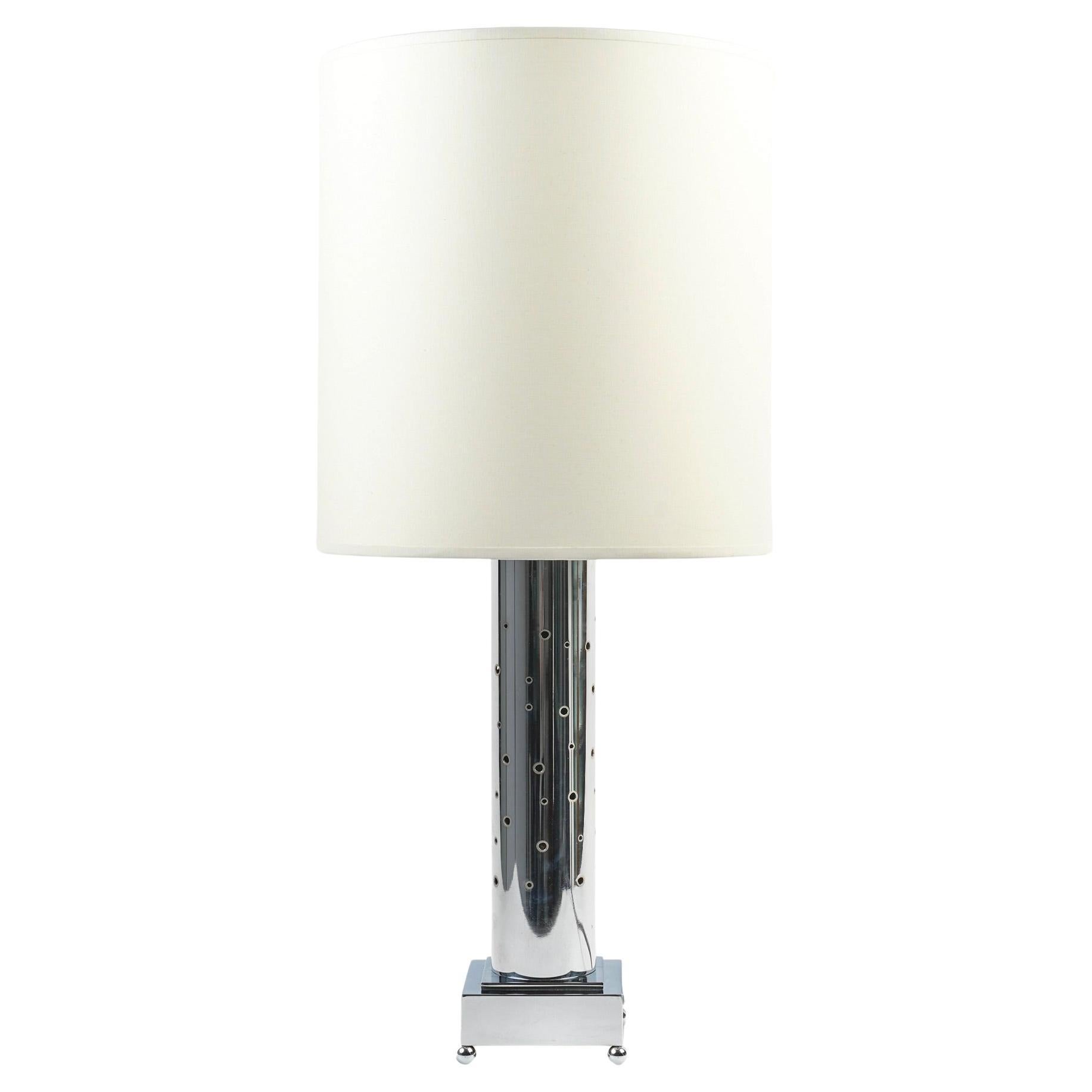 Composed of a cylindrical base in silver-plated chrome embellished with rounded cavities of varying size all over the surface, the cavities are encircled by gold-plated brass that lets light through when the base is lit.
The base rests on a