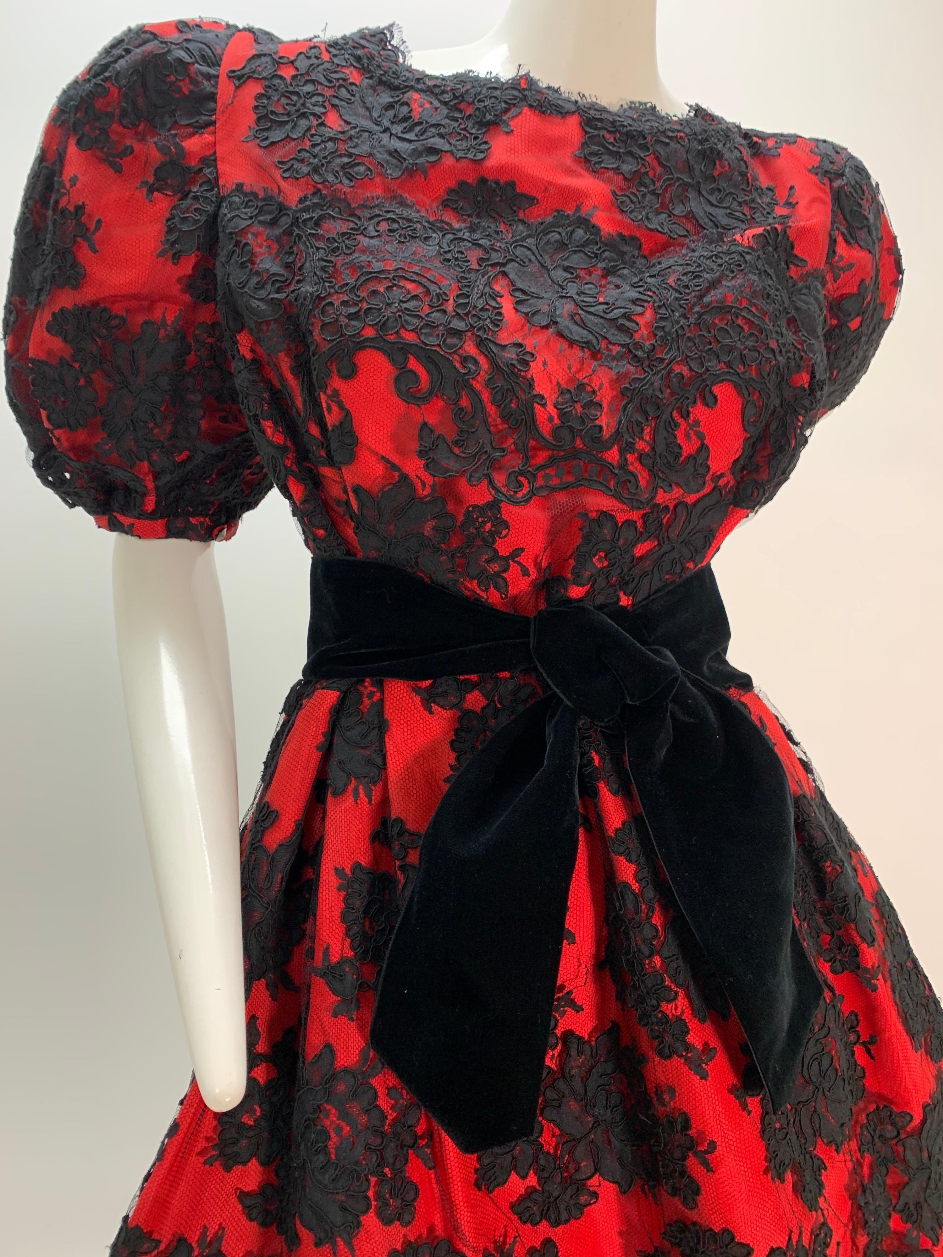 A beautiful and dramatic 1980s Pauline Trigere red silk taffeta cocktail dress with gorgeous black lace overlay: Puff-sleeved with a black velvet belt tied at center front, this bold ensemble features a narrow underskirt with a fuller