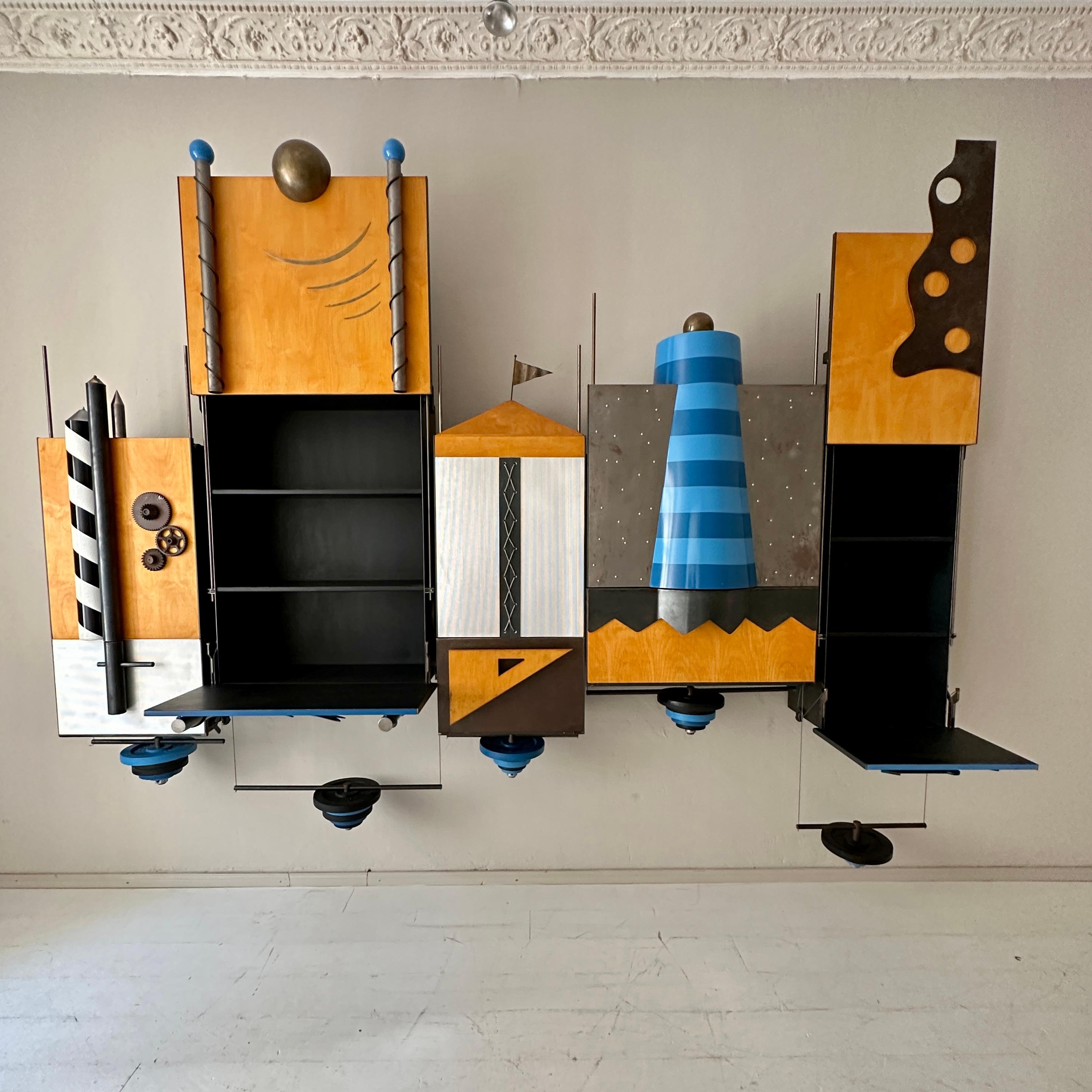 This 1980s Post-Modern One of a Kind Big Wall-Unit was made in 
metal, lacquered plywood, brass and lacquered plastic.
It is in blue, white, black and ocher beige.
The fantastic mechanism with the gym weights makes it super easy to open 1 of the 5