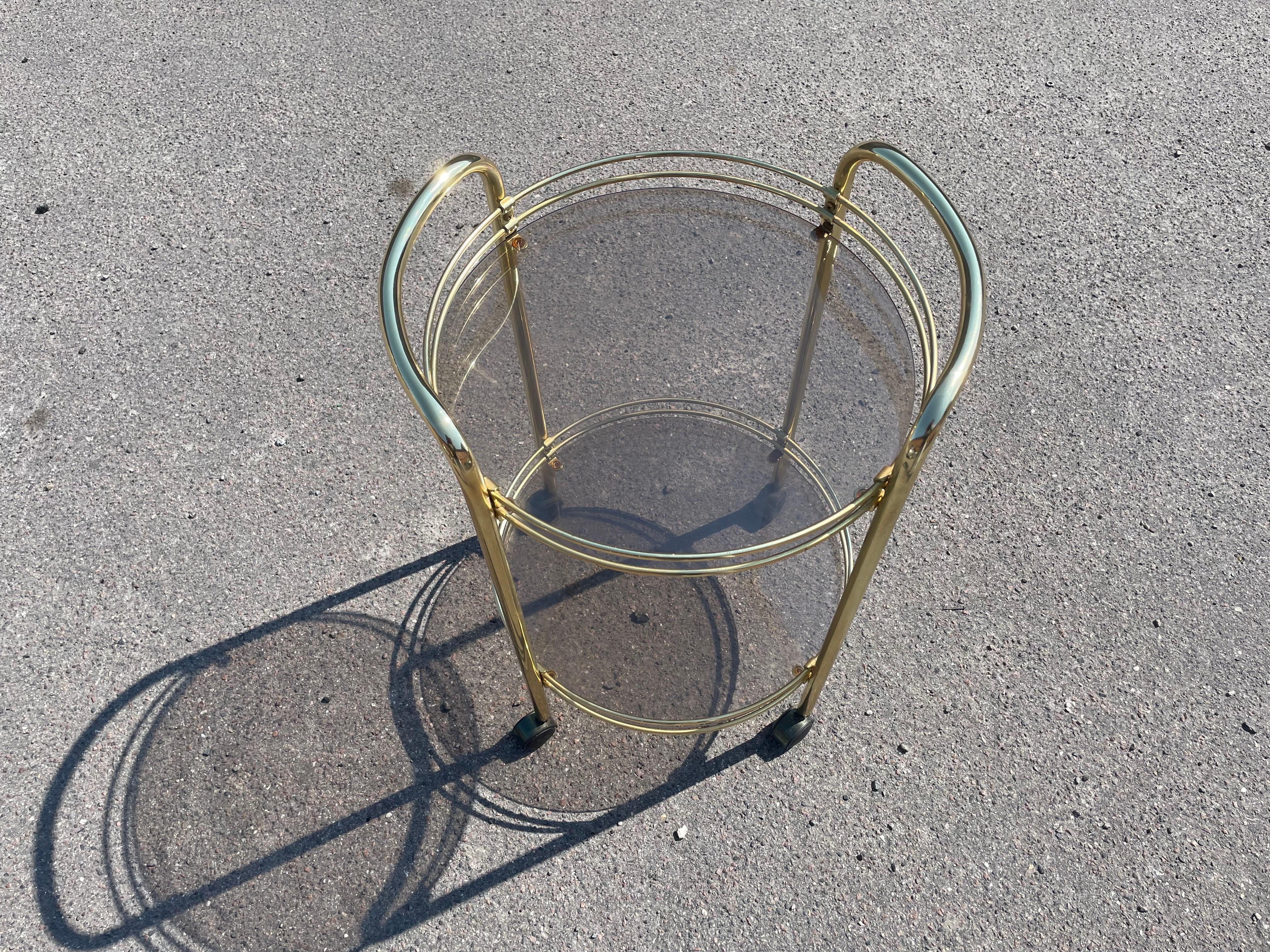 epitome of 1980s luxury with this Danish golden bar cart, a stunning piece that radiates timeless elegance. In perfect condition, this cart features a lustrous gold frame and two sophisticated shelves fitted with toned glass.The glamorous appeal of