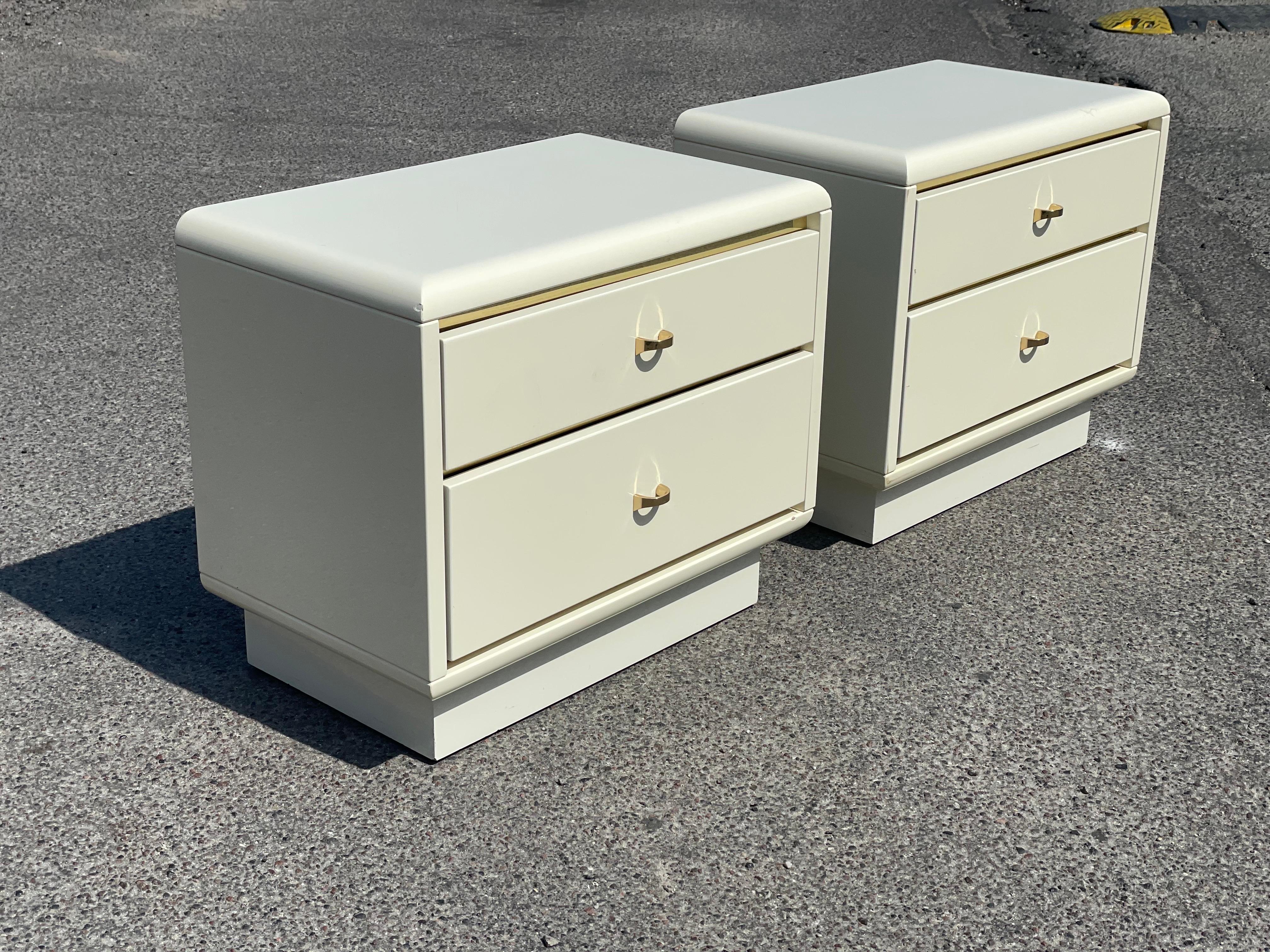 Vintage set of 1980s postmodern nightstands. Finished in a luxurious lacquer cream with striking brass accents, each nightstand boasts two spacious drawers for ample storage. Their bold, geometric design reflects the daring aesthetic of
