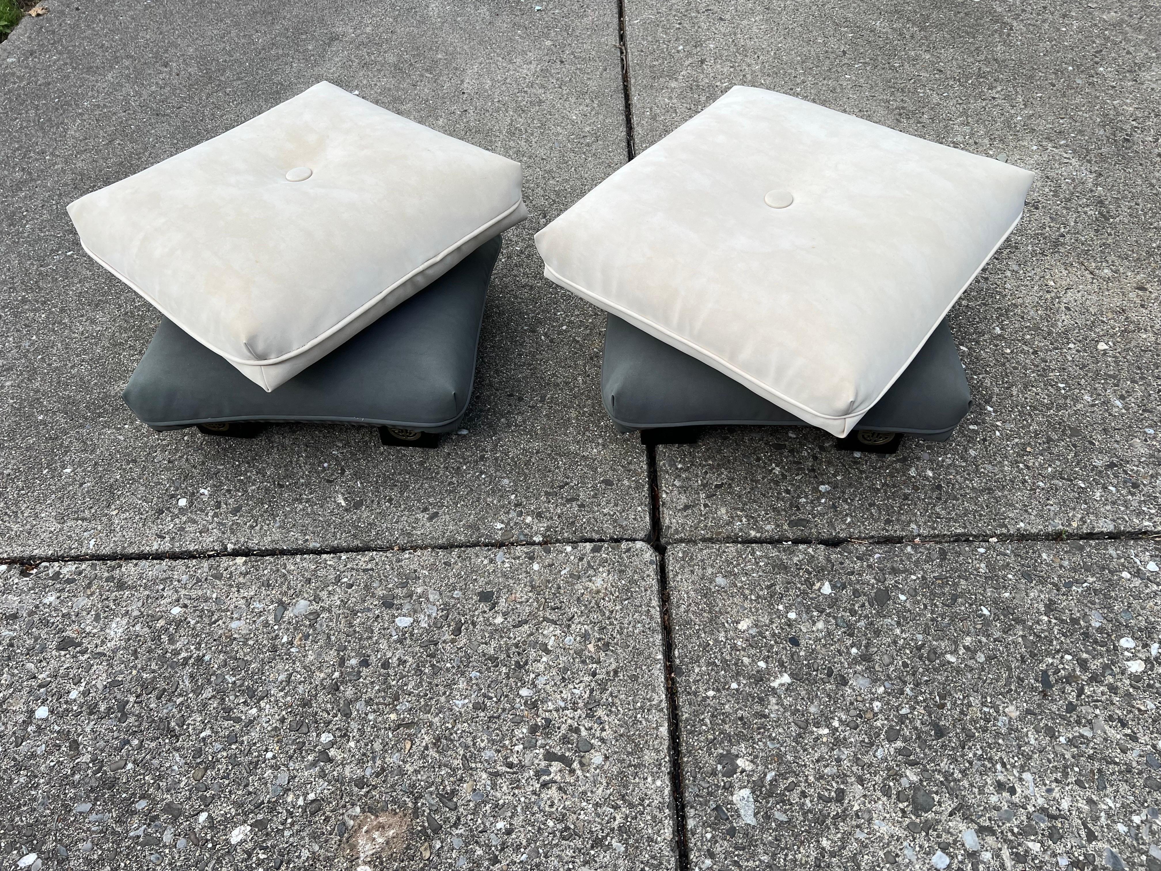 A pair of swivel ottomans made of ultrasuede from the 1980s.

Each ottoman has the top part which is in beige white color and the bottom base is in grayish green color. The legs of the ottoman has the brass oriental details.