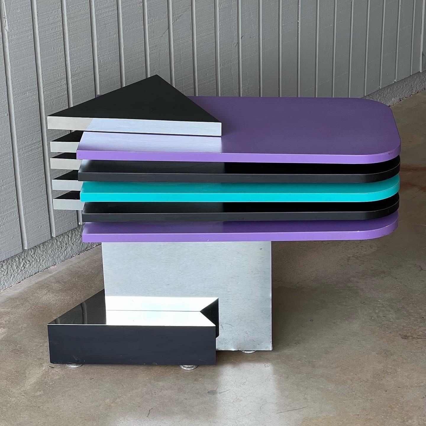 1980s-1990s post modern swivel side table or display stand. Wood with chrome, black, purple and turquoise laminate. The laminate tops swivel 360 degrees. There is very minor surface wear to the laminate. The chrome mirror pieces have some dents,
