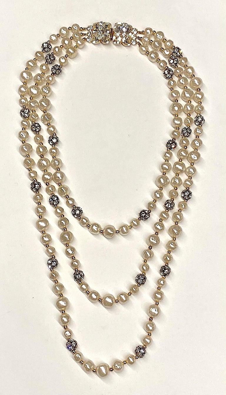 A stunning triple stand faux  pearl and rhinestone bead necklace from the 1980s. The faux pearls are a creamy off white in color and Baroque pearl style in three sizes of 10, 12, and 14 mm. Additionally, every five pearls there is a 12 mm rhinestone