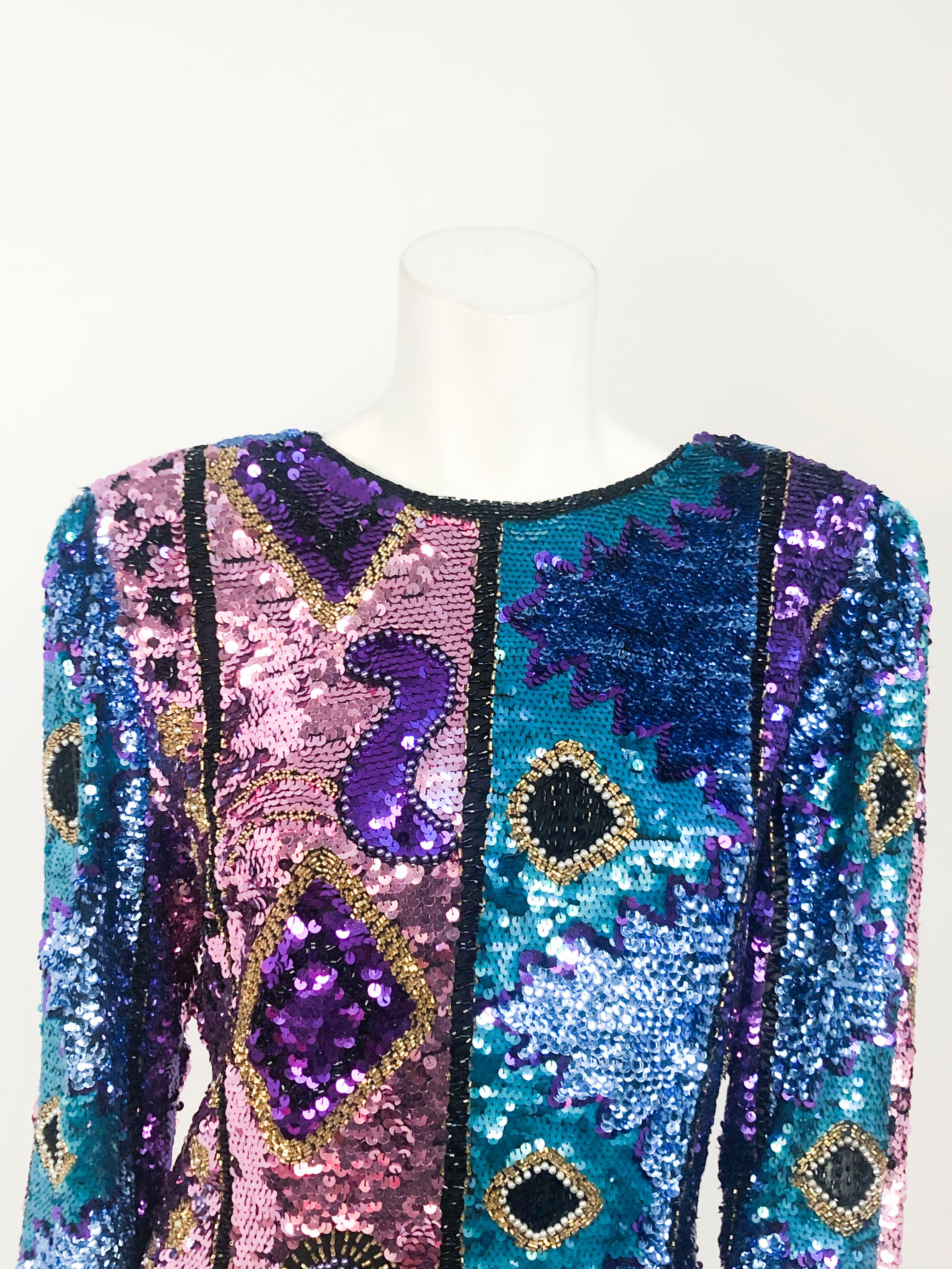 1980s sequin and beaded top with tones of pink, blue, purple, and light blue configured in an abstract/zig zag pattern. The shoulders are structured, and the neckline is high in the front and a V-neck in the back. The garment base is made of a silk