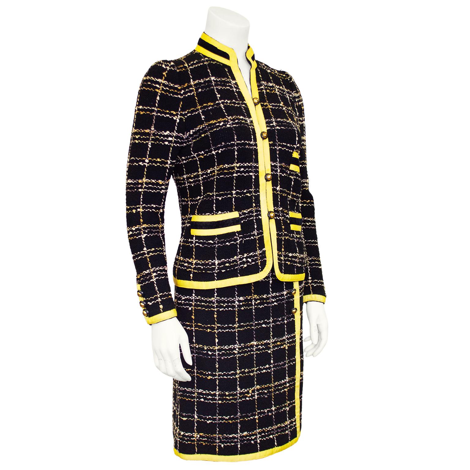 1980s Adolfo skirt suit. Black tweedy knit with grey, taupe and cream plaid and butter yellow grosgrain trim. Jacket features a Mandarin collar and horizontal slit pockets with yellow grosgrain and black velvet trim. Skirt is classic highwaisted