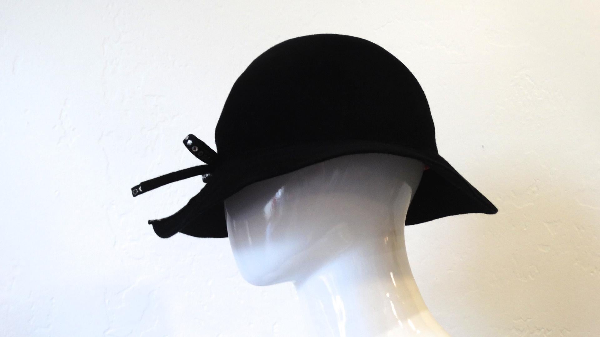 Le plus adorable chapeau des années 80 est là ! Fabriqué en laine noire, ce chapeau derby à large bord présente une fente unique sur le bord et la couronne et est décoré d'un nœud en strass. Des strass bordent également le côté droit de la fente. Le