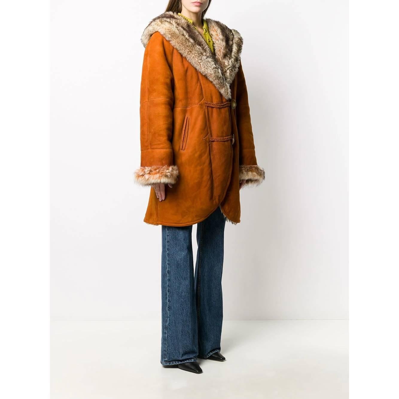 A.N.G.E.L.O. Cappotto vintage Cult in camoscio marrone arancione con pelliccia artificiale beige. Modello con cappuccio e collo a scialle. Abbottonatura frontale decentrata con alamari, maniche lunghe, due tasche frontali e orli