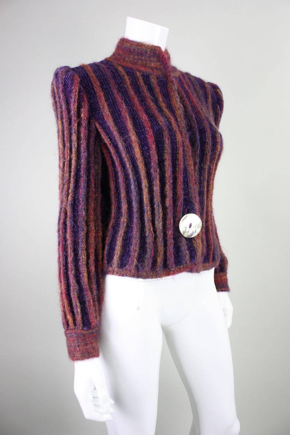 Vintage cardigan from Ann Caron by Annette Pyes dates to the 1980's.  It is made of a striped mixture of yarns of different hues of pink and purple.  Mock neck.  Large shell button at center front waist  and smaller button at neck.  Padded