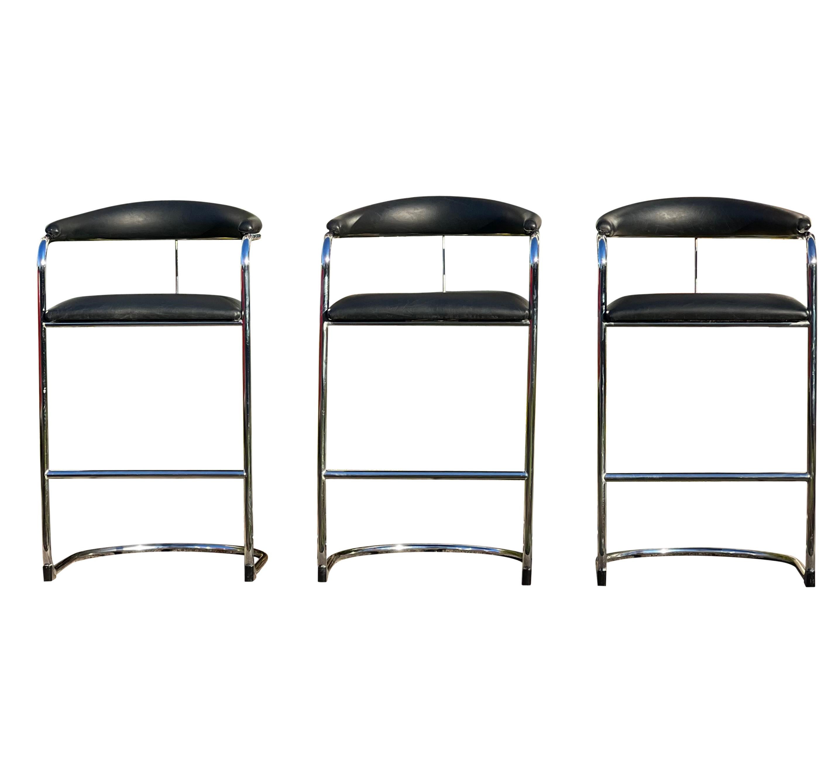 Later edition cantilever chrome bar stools designed by Anton Lorenz for Thonet in 1929.  Stools feature black faux leather upholstered seat and backrest with chrome-plated tubular steel frame and black stabilizers. All three stools are in very good
