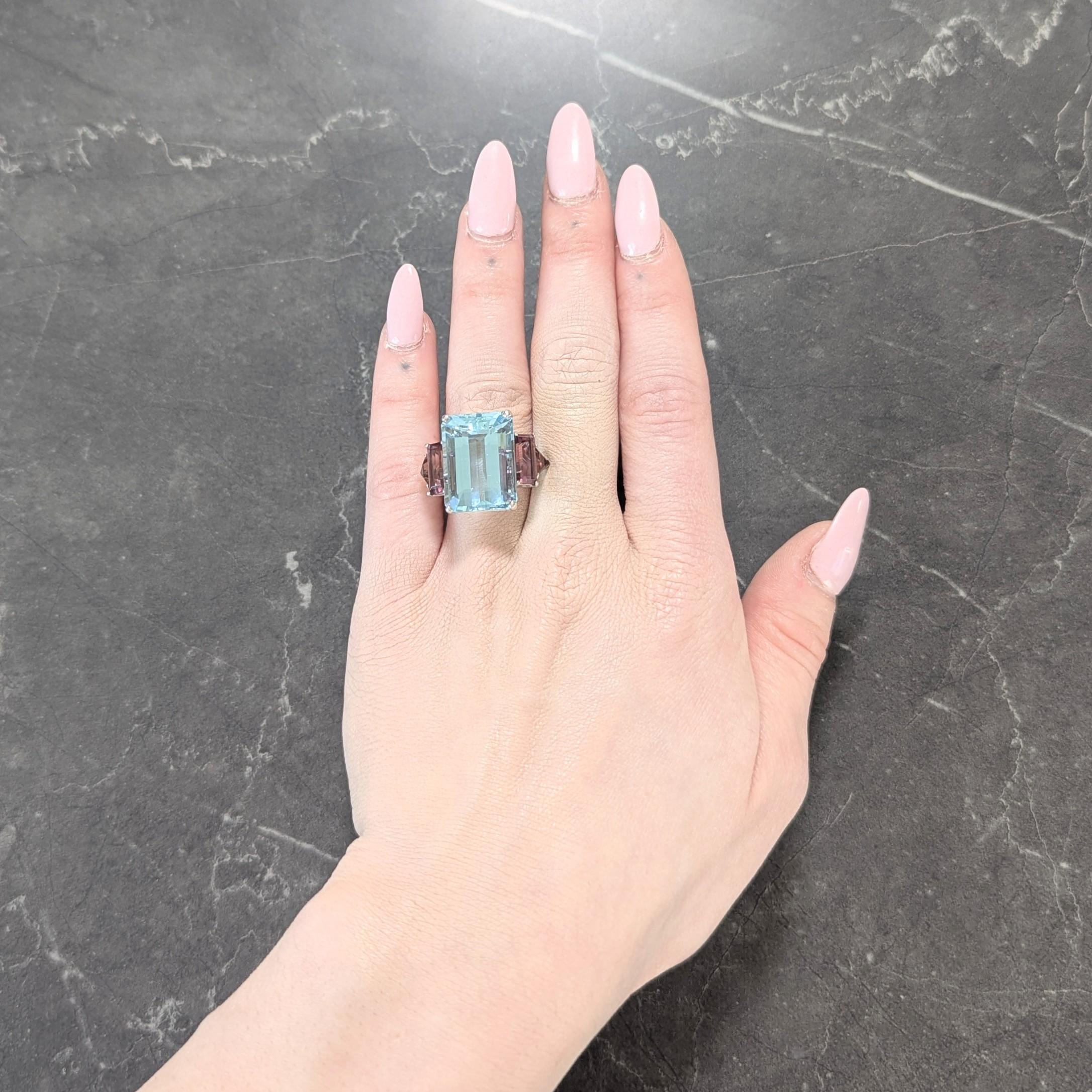 Centering an emerald cut aquamarine weighing approximately 20.00 carats total
Transparent light blue in color - prong set in tall basket flanked by tourmalines
Baguette and trillion cut measuring 4.5 x 10.0 and 5.0 x 6.0 mm, respectively
Transparent