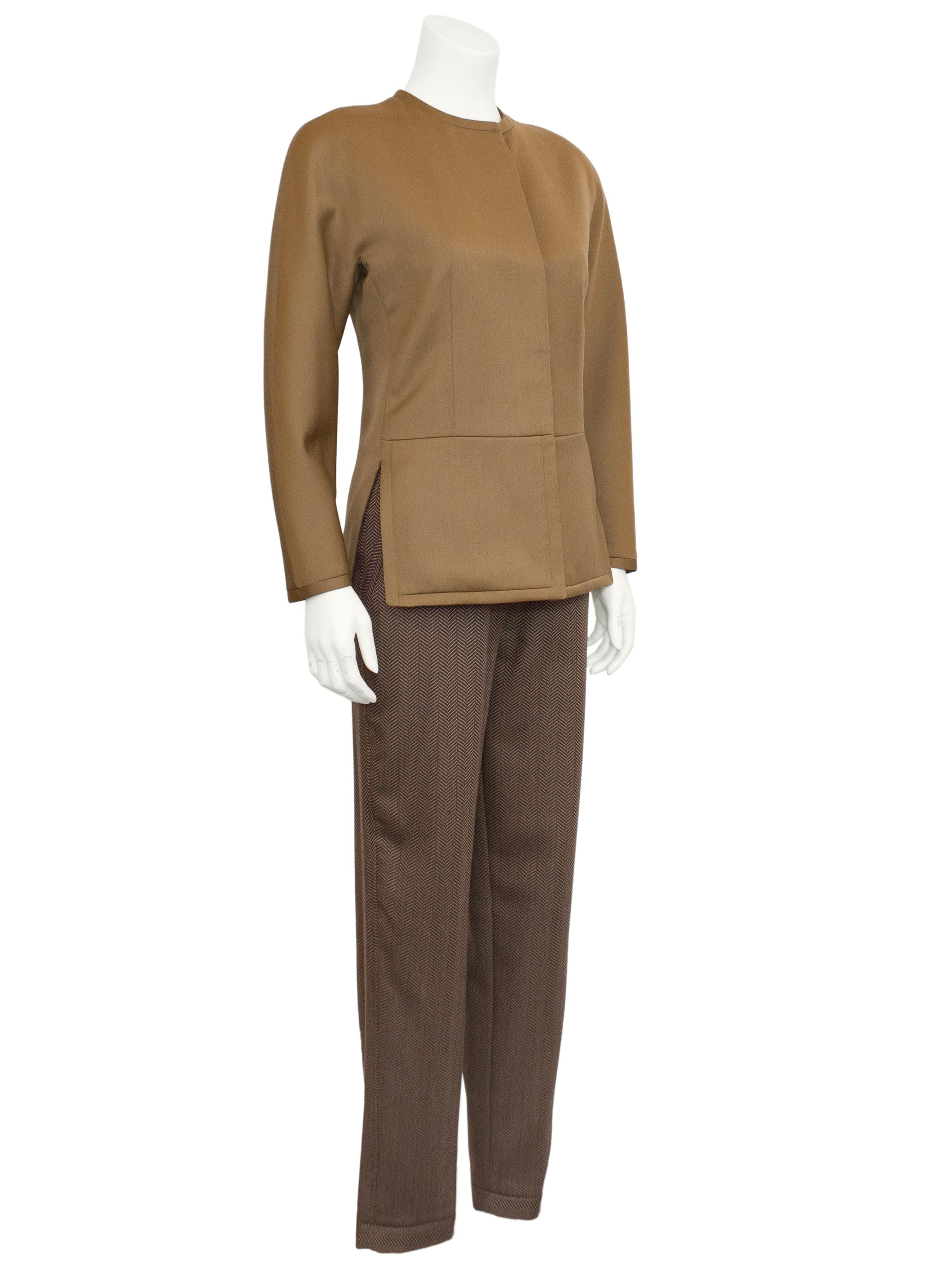 Super chic Armani pants suit from the 1980s. The brown collarless wool gabardine jacket has rounded shoulders with structured shoulder pads and darts down the front from the bust to the waist. The jacket buttons up the front under a placket and