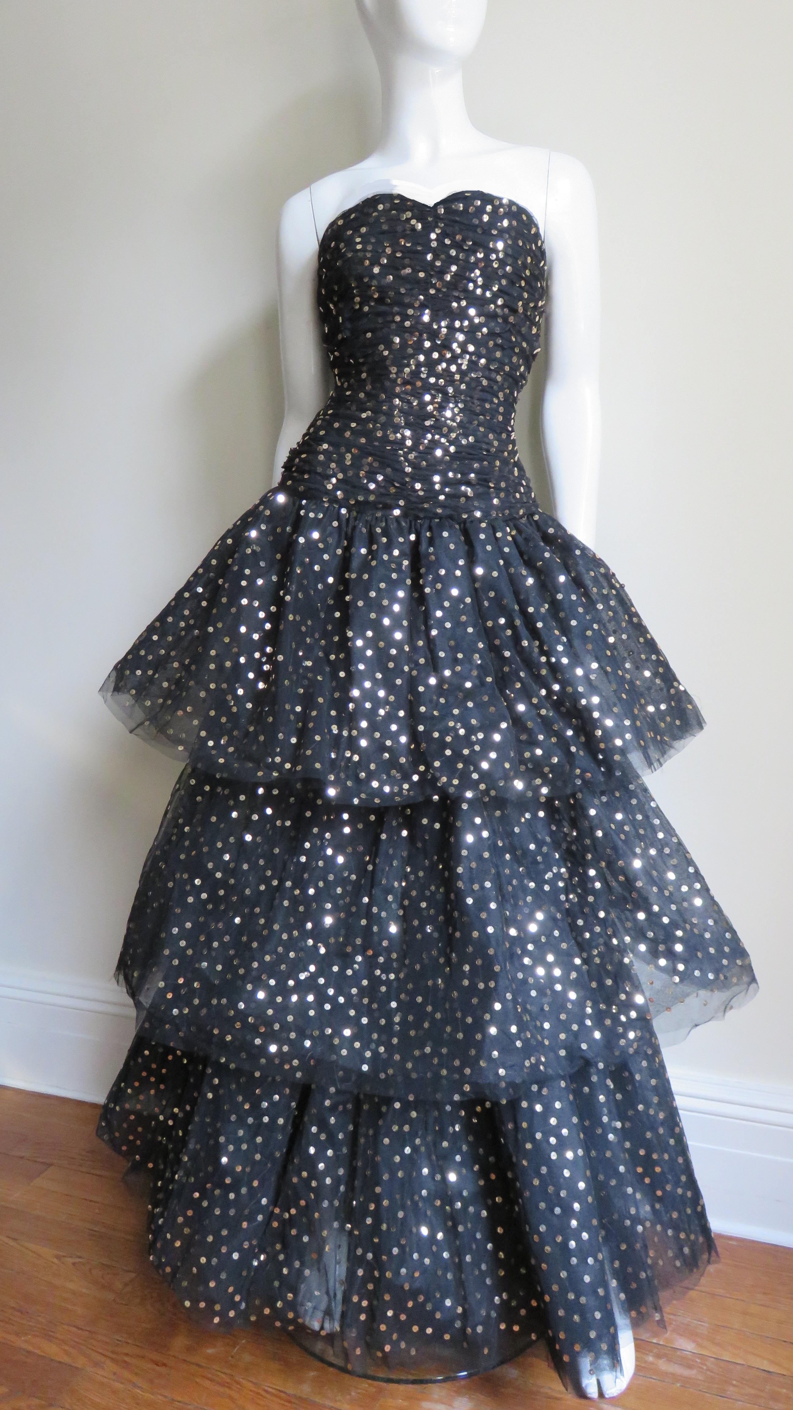 A sunning gown from Arnold Scassi consisting of layers of sequin dotted black tulle. The bodice is boned, horizontally ruched and has a drop waist. The skirt is layered in three lengths creating a full skirt and has additional layers of tulle