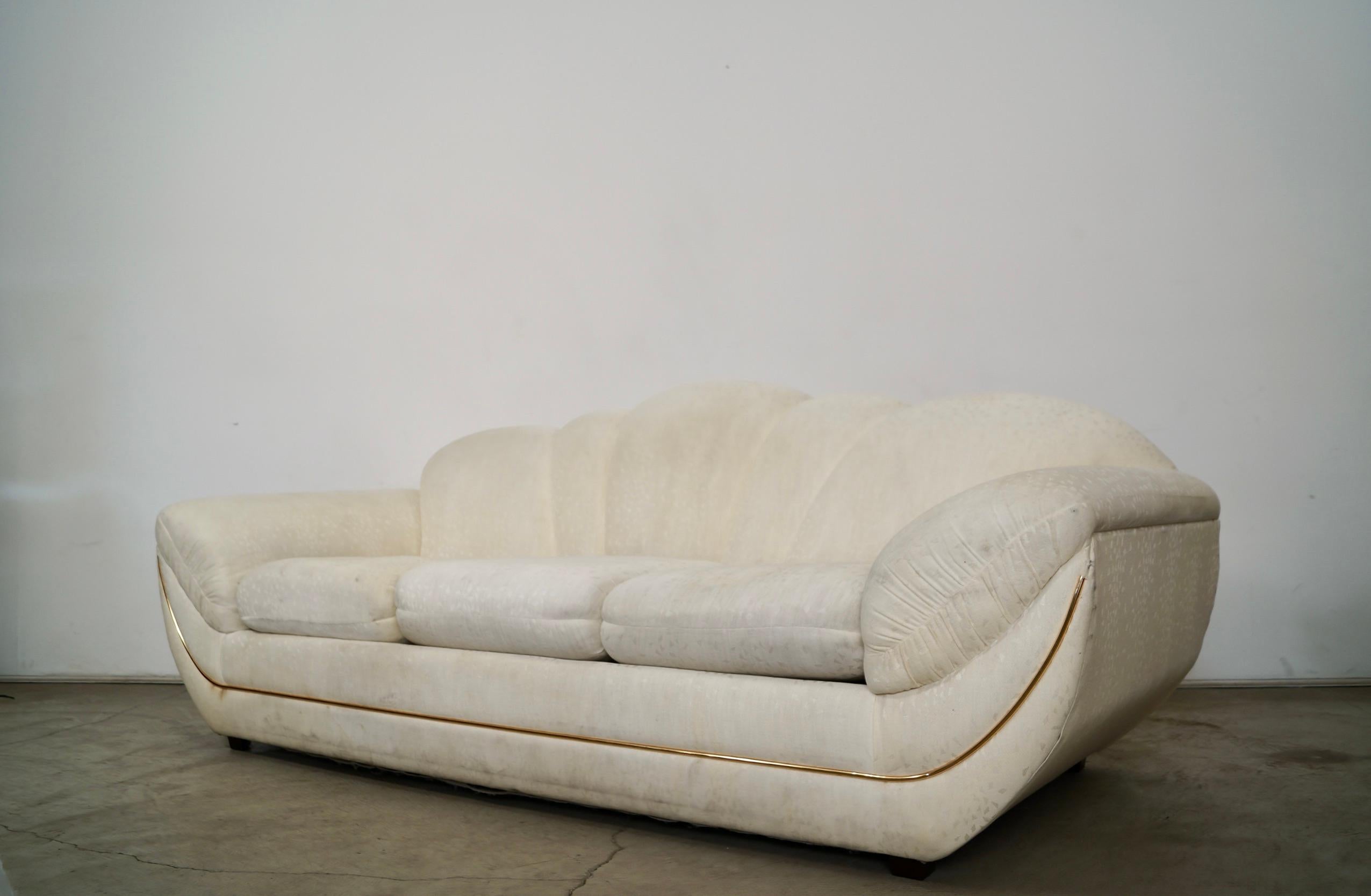 Vintage 1980's Art Deco sofa for sale. Manufactured here in the US by Bassett Furniture, and is a really high-quality couch. It has an amazing and unique gondola design with a long brass trim inserted into the frame. It has the original vintage