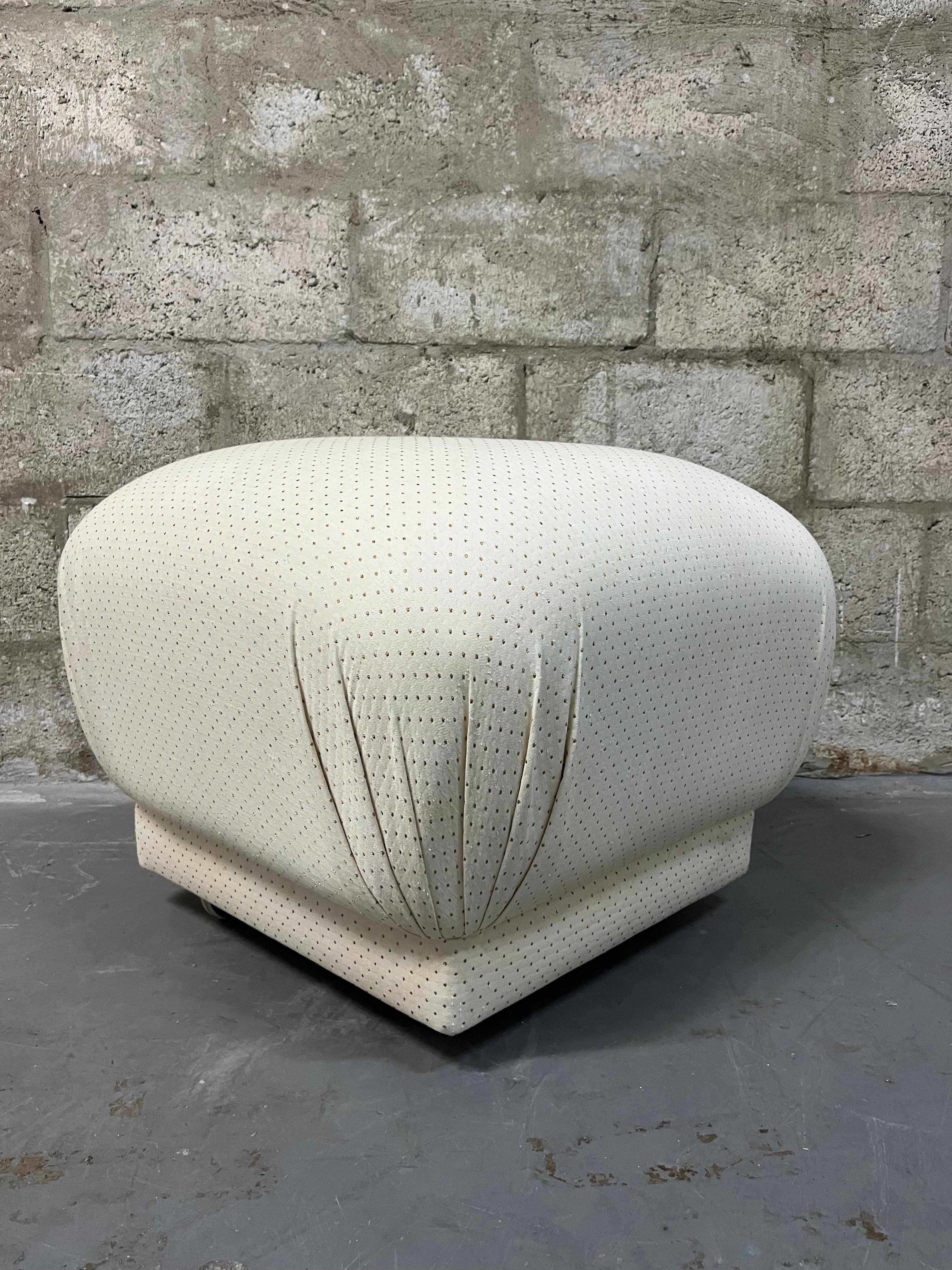 Vintage Hollywood Regency / 1980s Art Deco Revival  Souffle Ottoman Pouf With Casters in the Karl Springer Style.
Features the original cream upholstery with gold dots and brass plated casters for easier mobility. 
In excellent original condition
