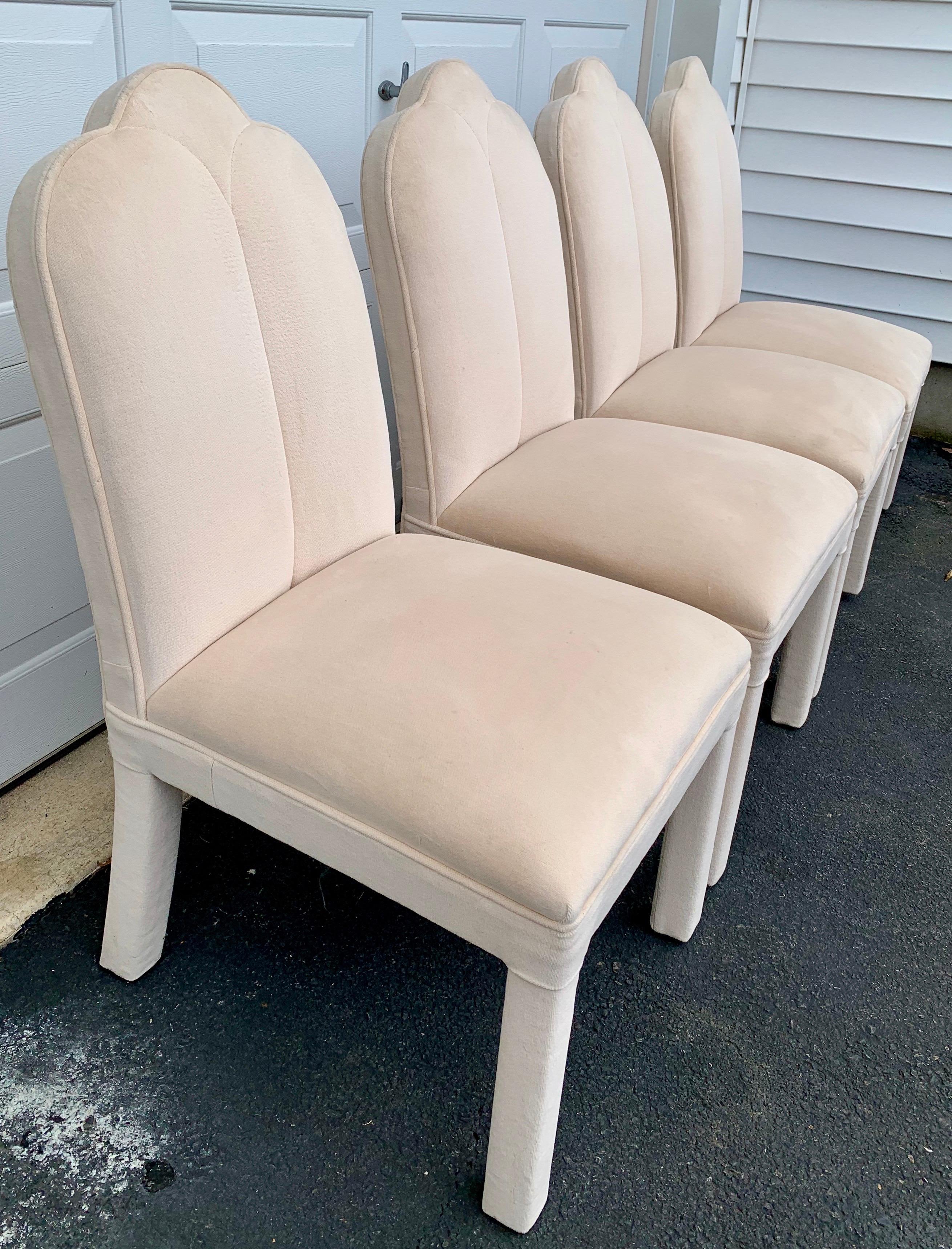 Set of four Art Deco style fully upholstered parsons dining chairs in the style of Milo Baughman. These sculptural chairs feature curved scalloped arched backs and original neutral sand/beige velvet upholstery.