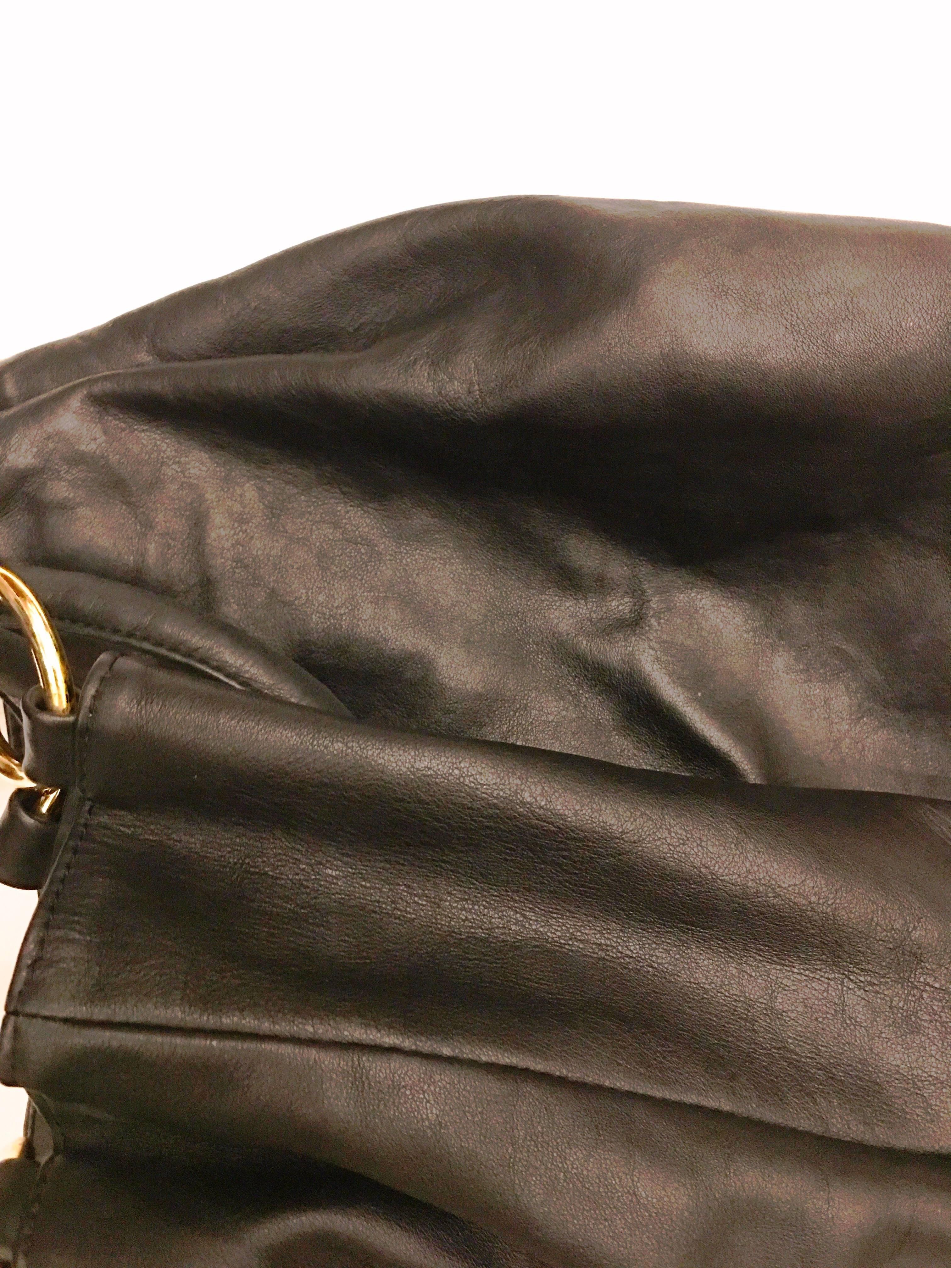 Black leather tote bag with 4 gold tone rings at handle. Handle is one single leather strap that loops around through the gold rings. Balmain crest and logo on gold tone disk at front of the bag. Two zipper pockets on inside of the bag. One larger,