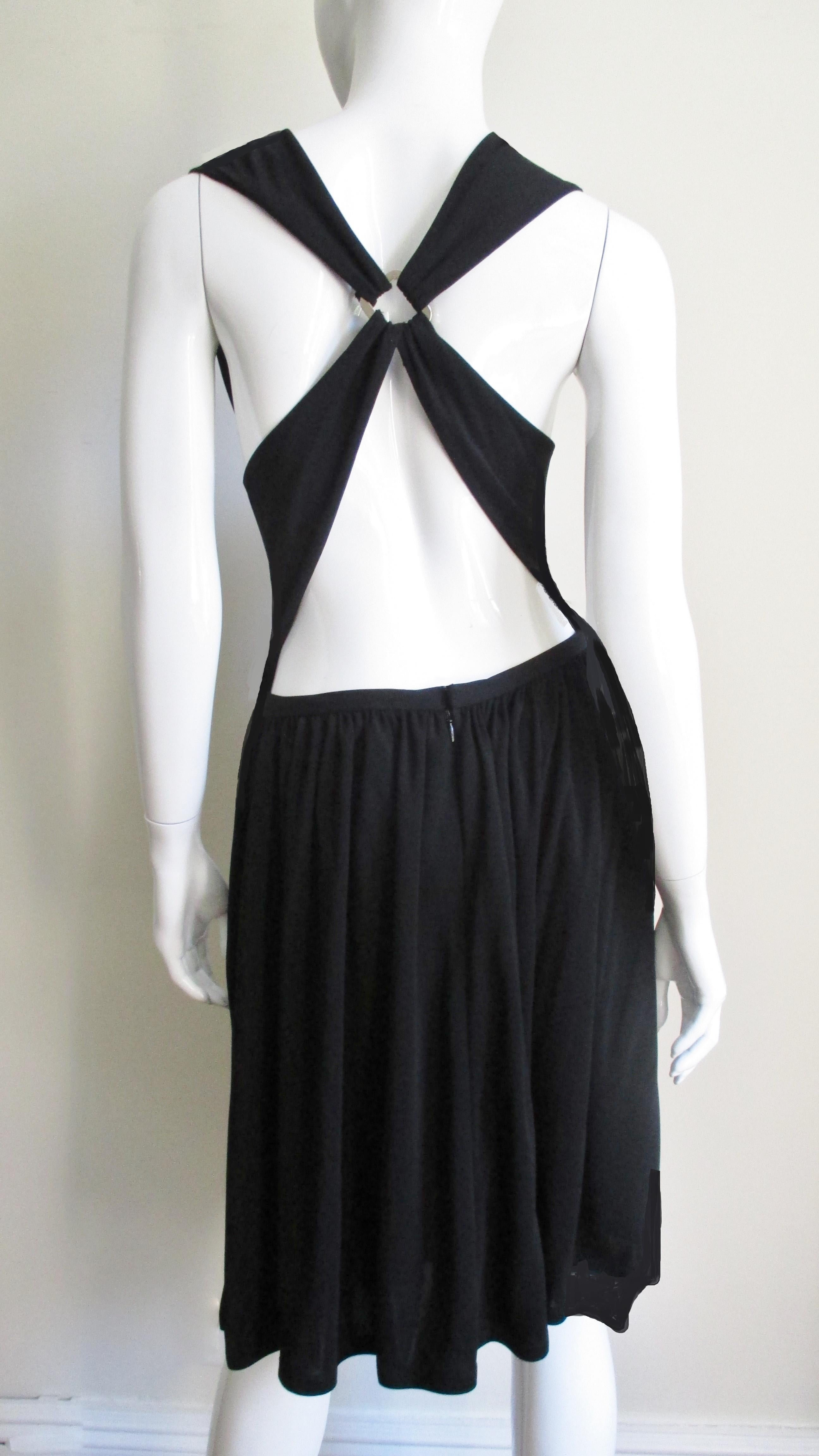 A simple black synthetic jersey dress from Bill Blass.  It has a fitted drop waist with a soft cowl V neckline.  A full skirt is gathered onto the bodice in the front and sits at the lower back.  The rest of the back is bare with the exception of 4