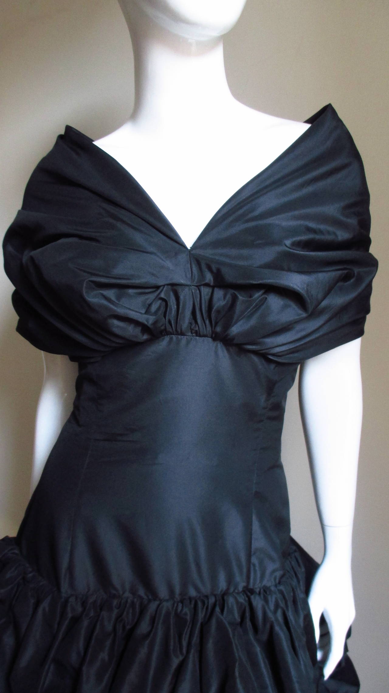 A fabulous black silk dress from Bill Blass.  The semi fitted bodice has a draped portrait collar wrapping around the shoulders, an inner boned corset  and a gathered skirt punctuated with elaborate white flower appliques.  The dress is silk lined