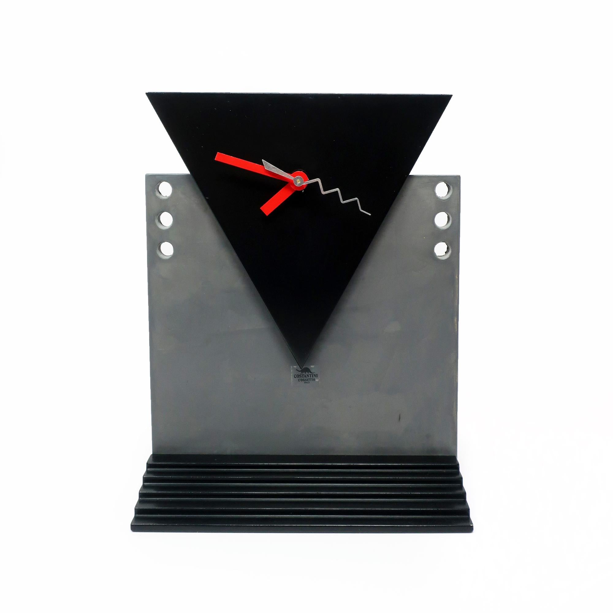 Manufactured by Costantini l’Ogetto in Italy during the 1980s and likely designed by Pietro d’Amato, this table or mantle clock has a glossy black stepped base, matte gray body, matte black face, and red and silver hands. The clock has a new